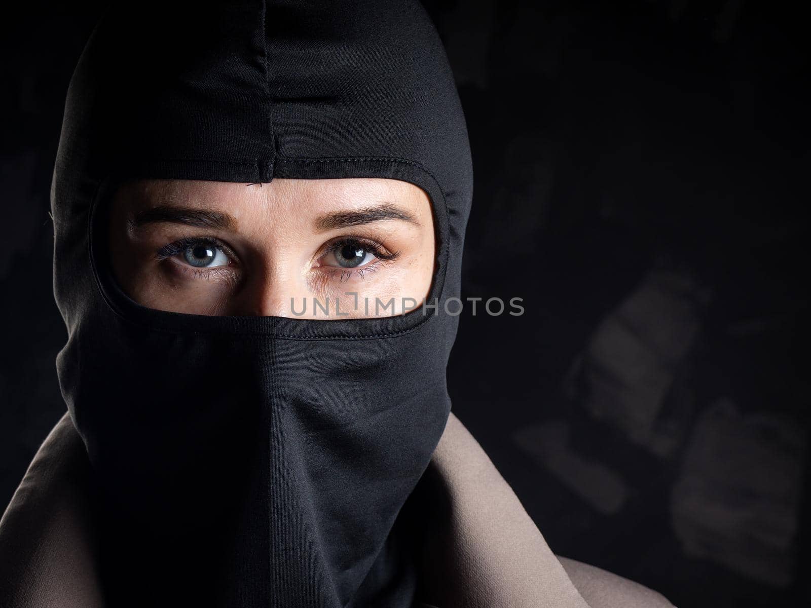 Portrait of a girl in a black balaclava and beige coat. Shot in the studio on a dark background.