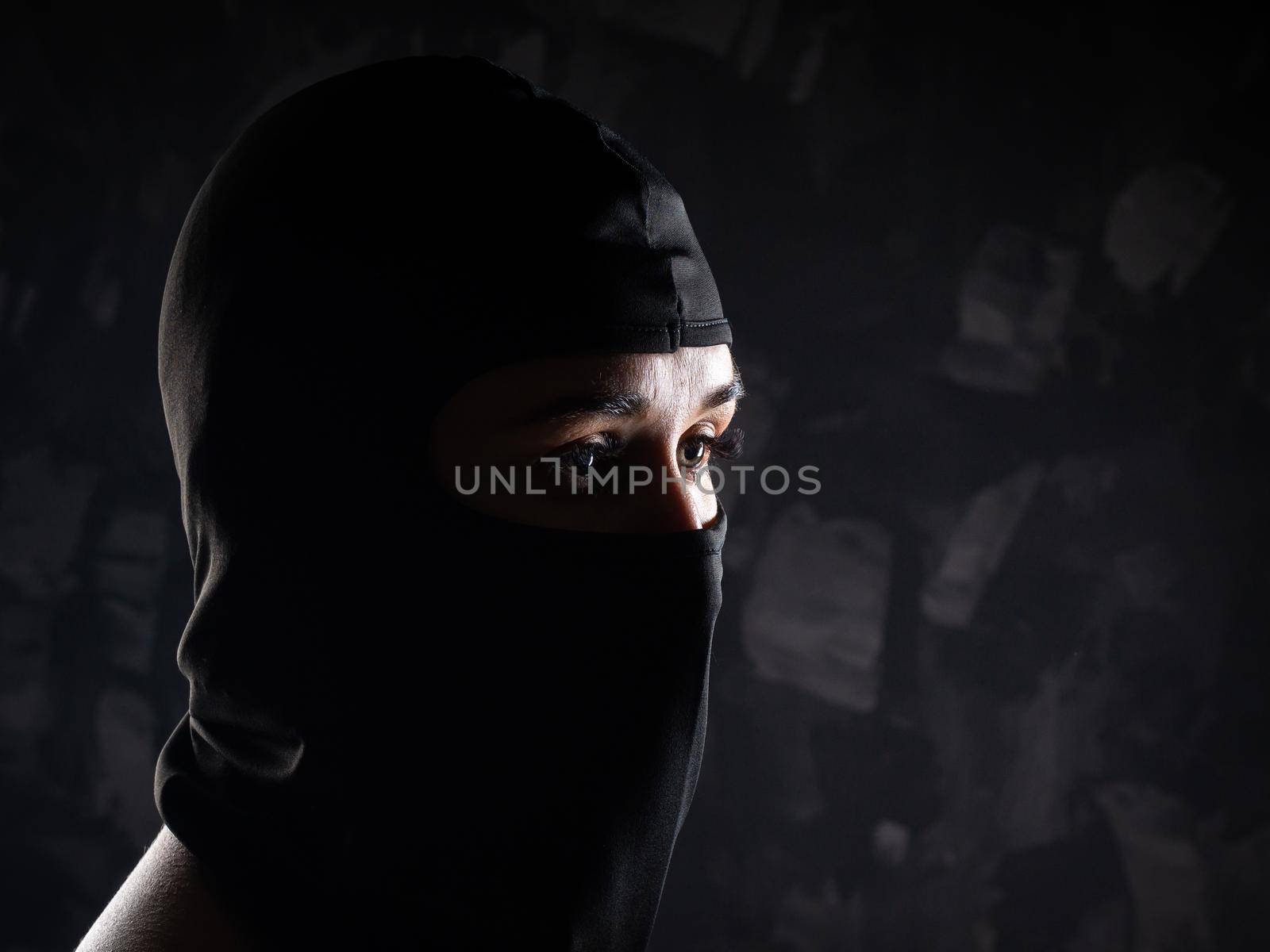 Portrait of a girl in a black balaclava and a black bra. Shot in the studio on a dark background.