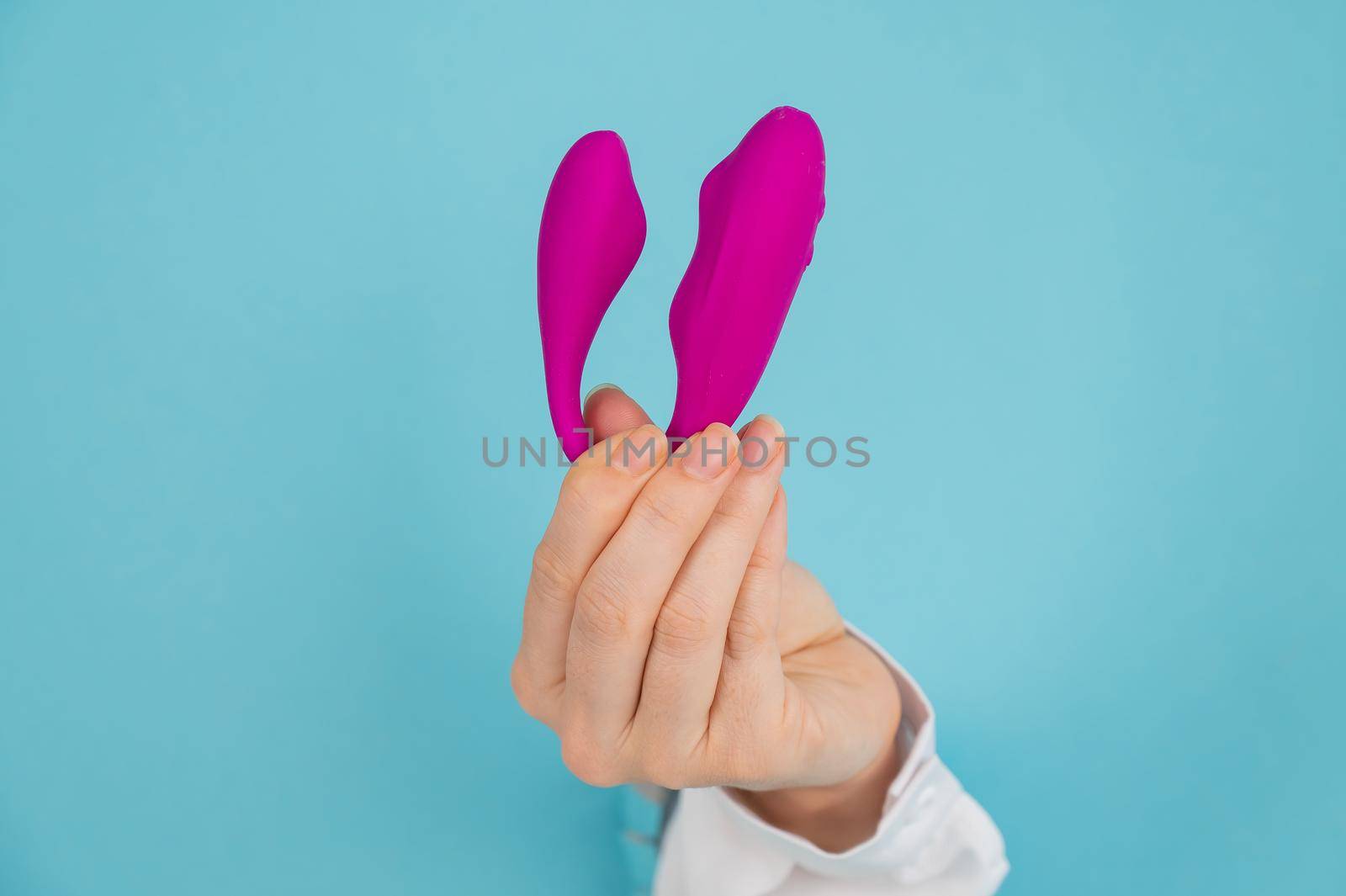 A woman's hand holds a pink sex toy through a hole in a paper blue background