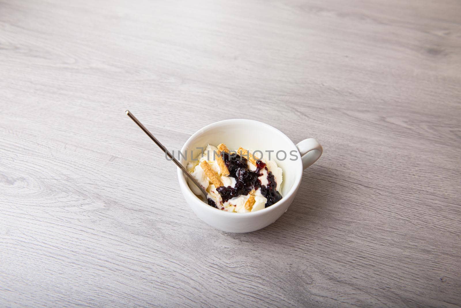 Vanilla ice cream with blackberry jam in a white cup on a wooden light background by marynkin