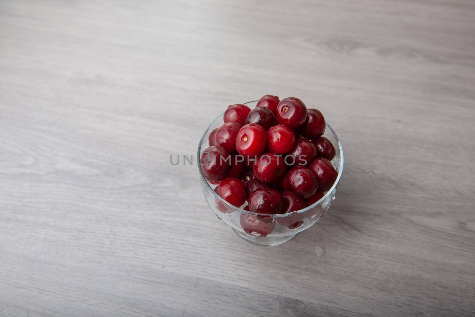 cherry in a glass bowl on a light wooden table by marynkin