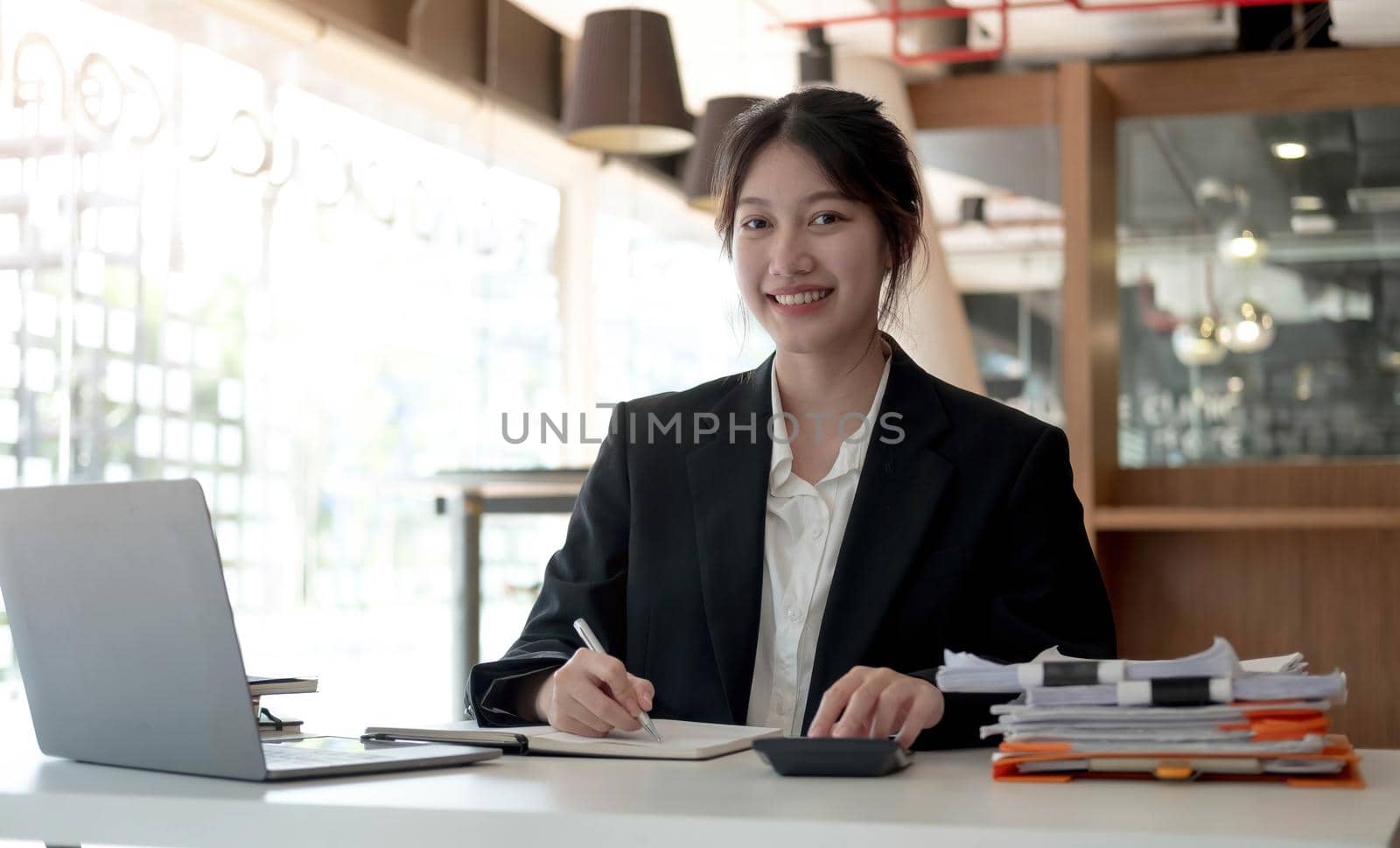 Beautiful smiling Asian woman working at the office, looking at the camera. by wichayada