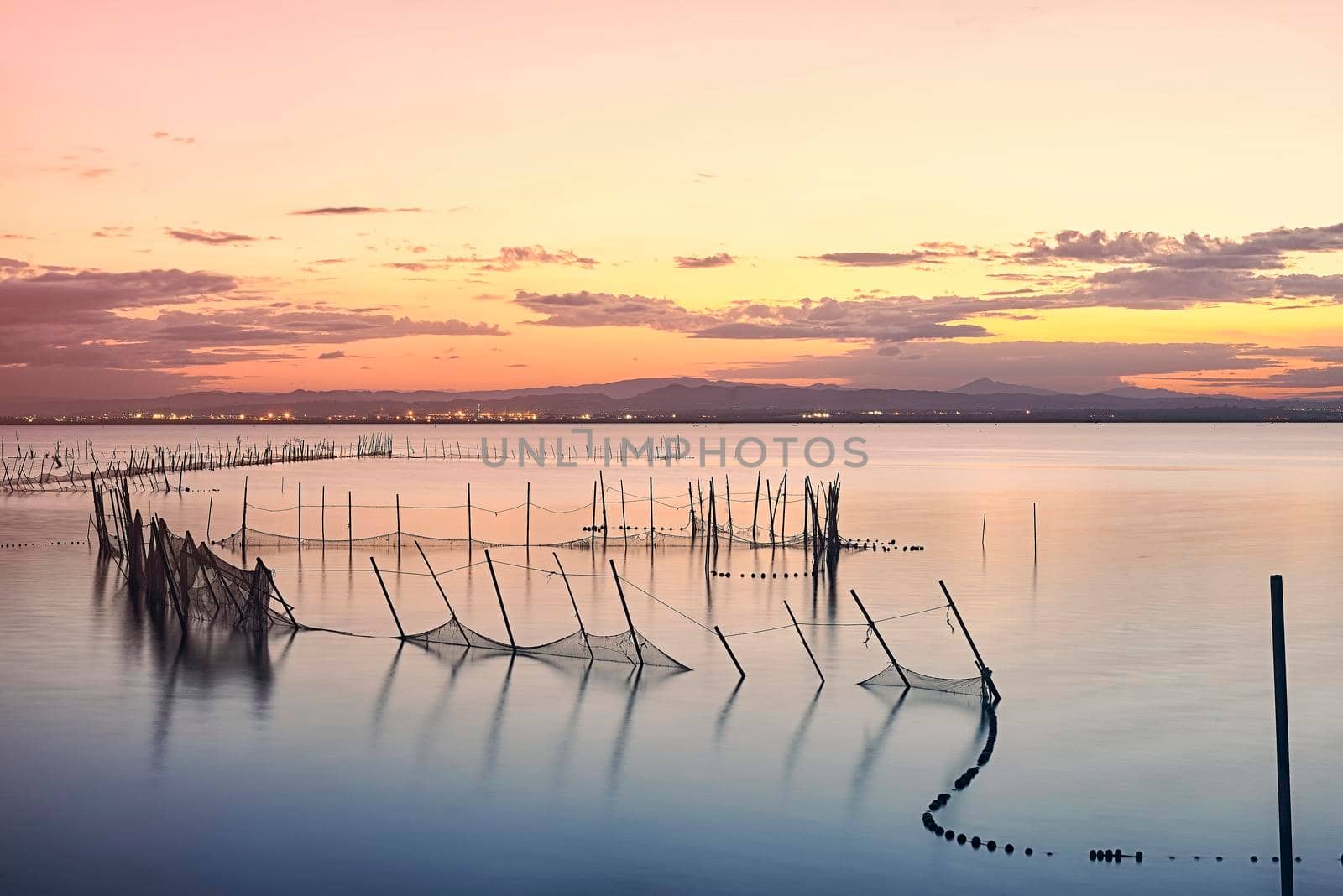 Sunset on the Valencia lagoon between the nets. Long exposure photography, orange and yellow tones. silk effect water.