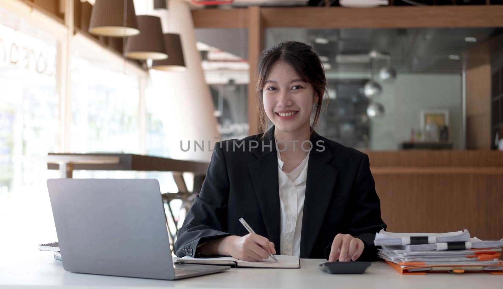 Beautiful smiling Asian woman working at the office, looking at the camera. by wichayada