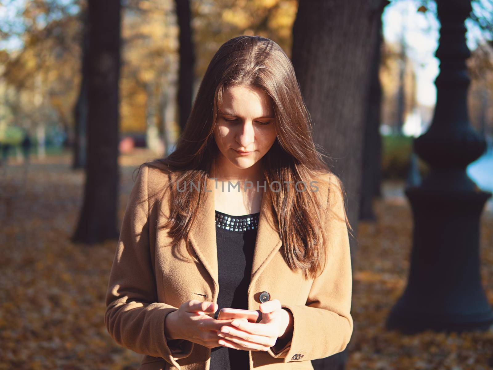 Beautiful teen girl in the Park, holding smartphone and chatting online on Internet. Young woman with long hair by NataBene