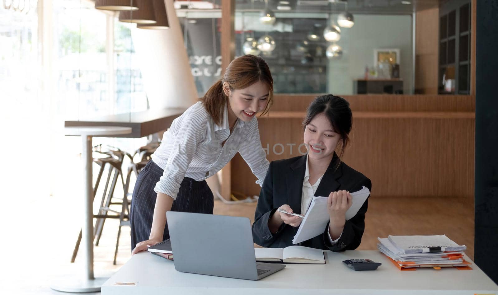 Two young asian women colleagues in smart casual wear planning business strategy together at the modern coworking space..
