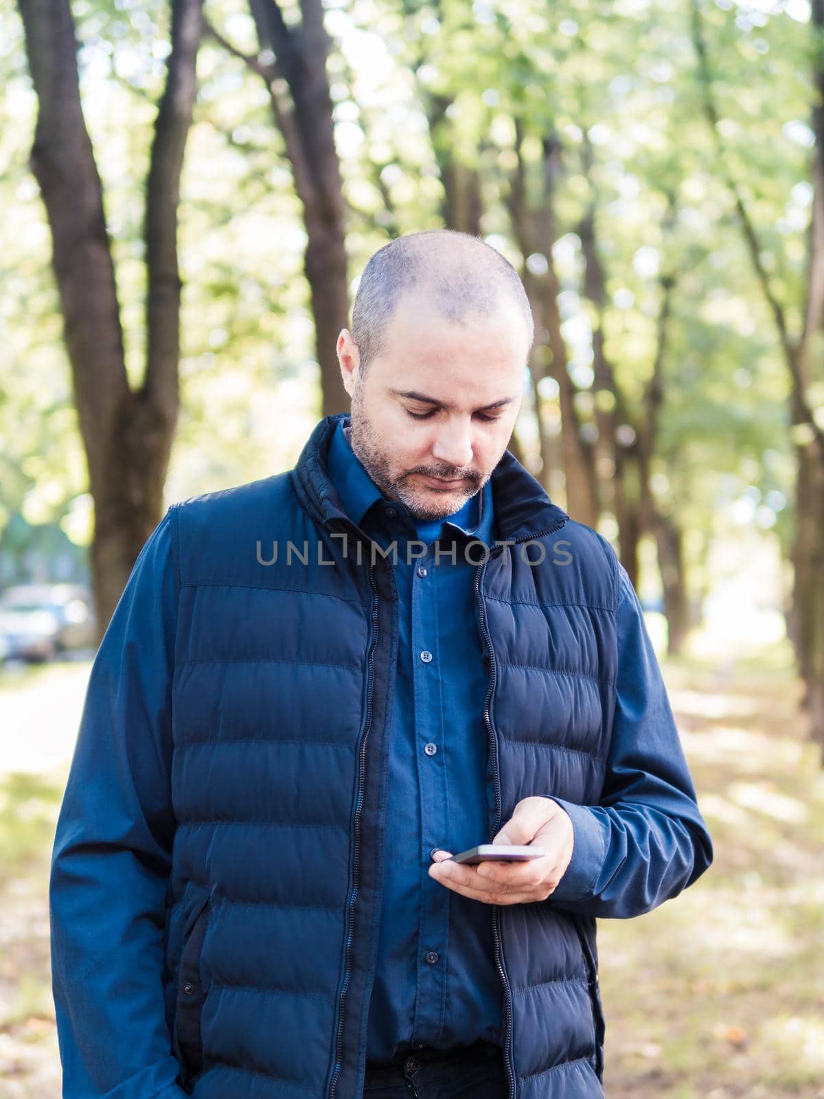 man is holding a phone, walking in the city Park, among the trees and looking at the smartphone.