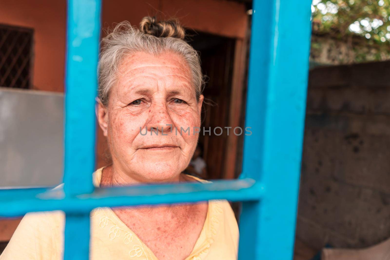 Elderly white latin woman with blue eyes at home looking at camera behind your metal gate