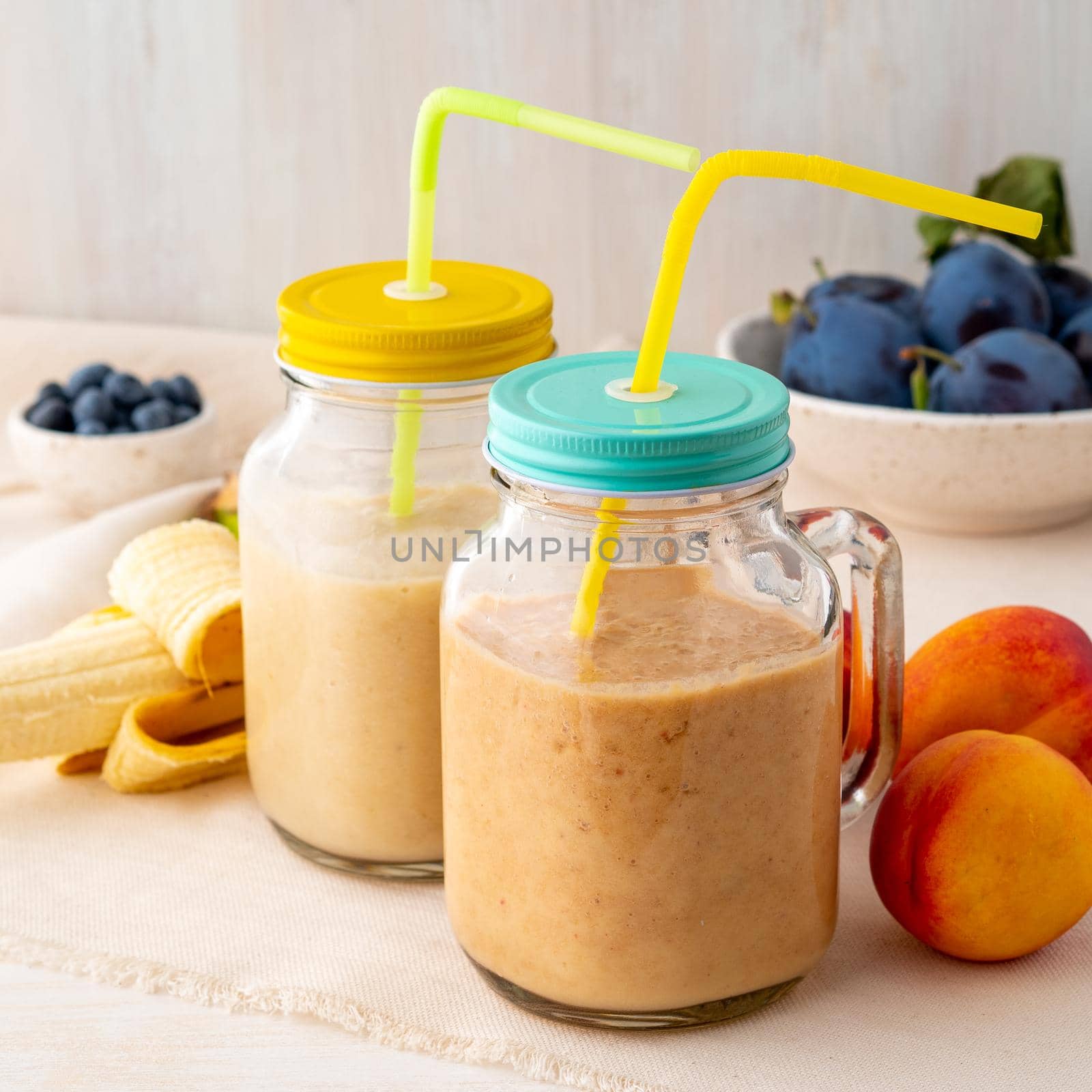 banana peach nectarine smoothie in two jars, fresh fruit milkshakes on the white rustic wooden table, side view