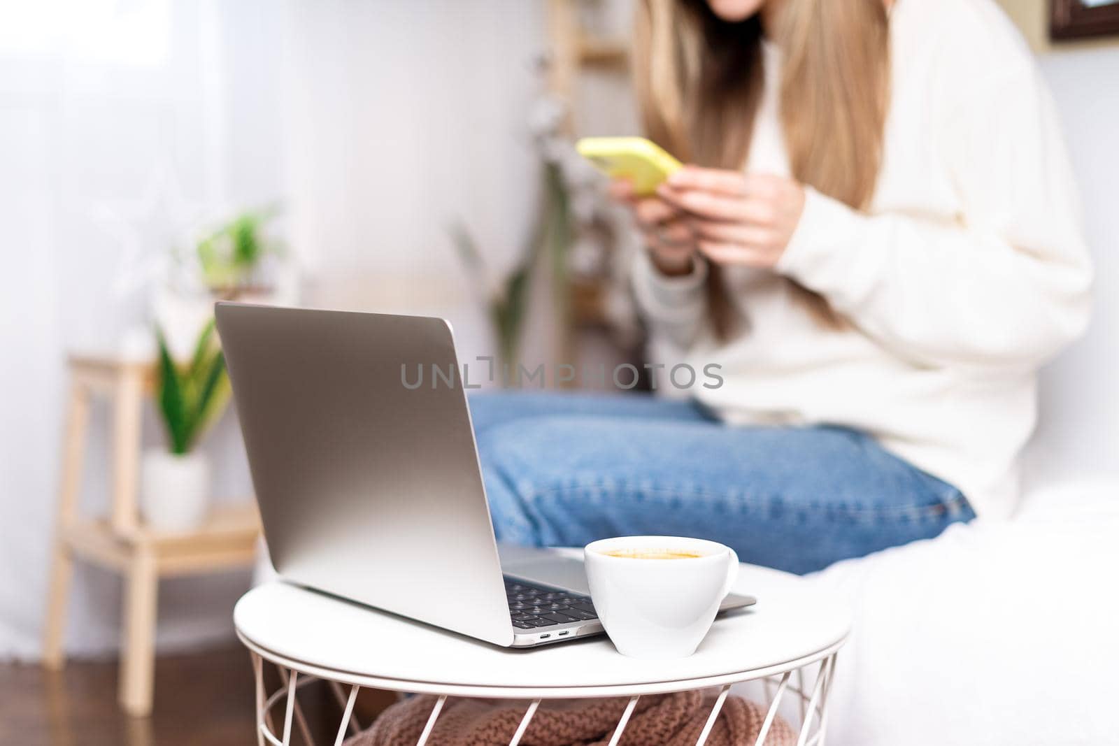 Freelance woman with laptop and cup of coffee using mobile phone and online shopping, sitting on the couch. Happy girl woking from home office. Distance learning online education and work.