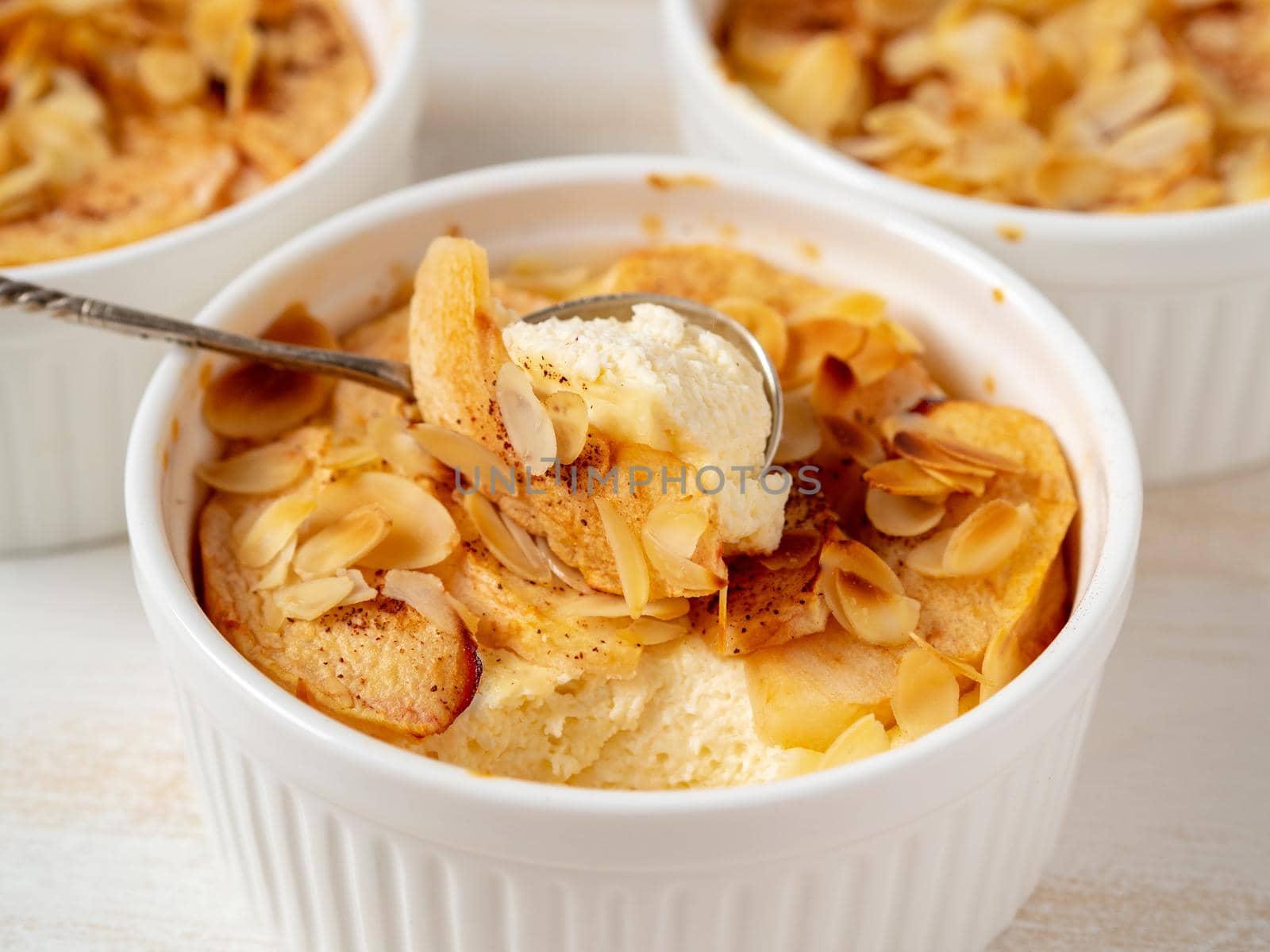 Cheesecake on white wooden table in kitchen. Delicate curd dessert with apples, almond flakes by NataBene