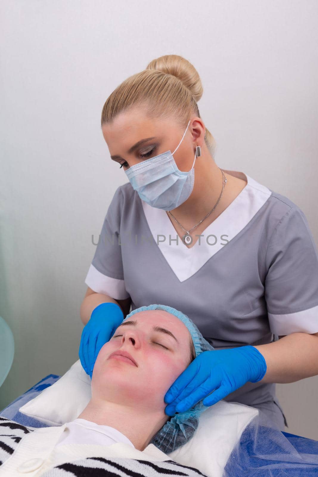 A female cosmetologist manually treats the patient's skin with a moisturizing and toning gel. by BY-_-BY