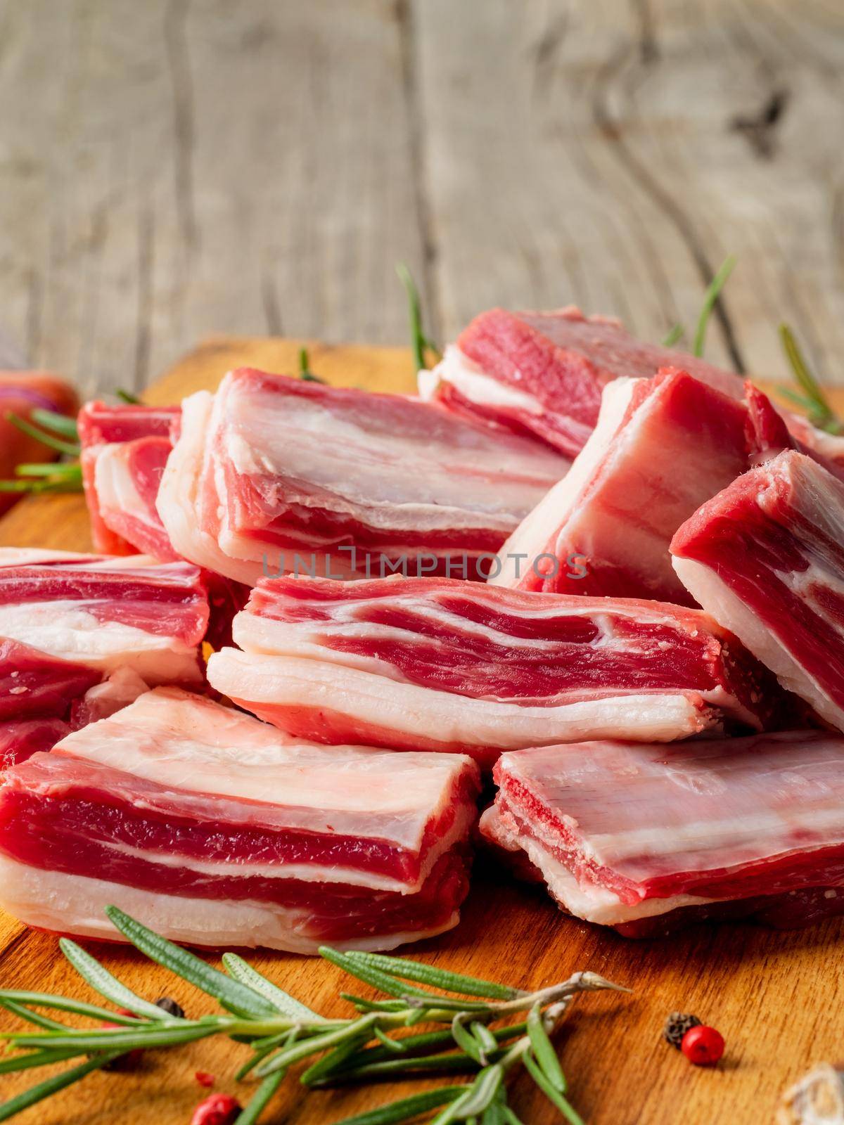 Small pieces of raw lamb ribs on wooden chopping Board on old rustic wooden background, side view, vertical