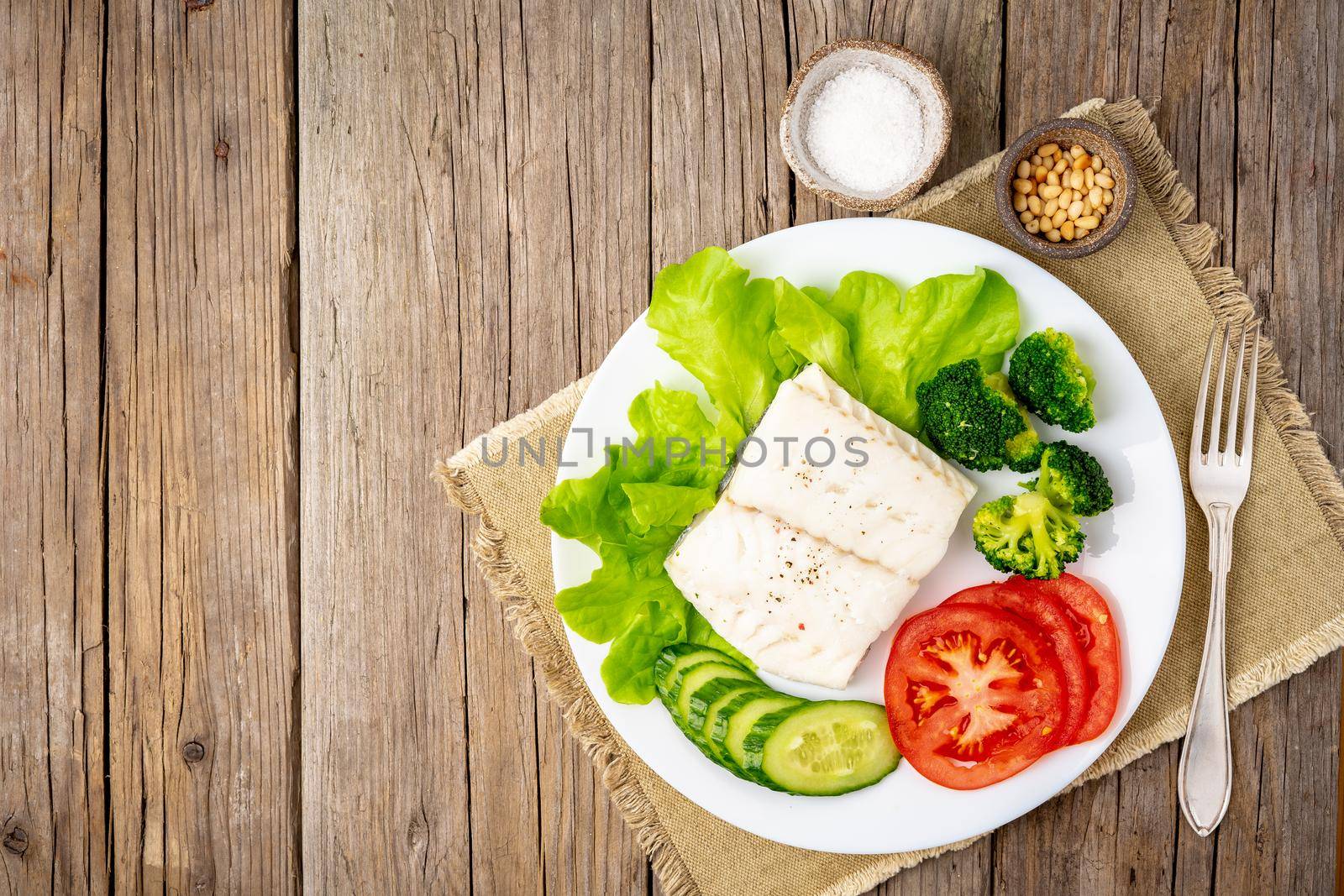 Steamed cod fish. Paleo, keto, fodmap healthy diet with vegetables on white plate on white table, side view.