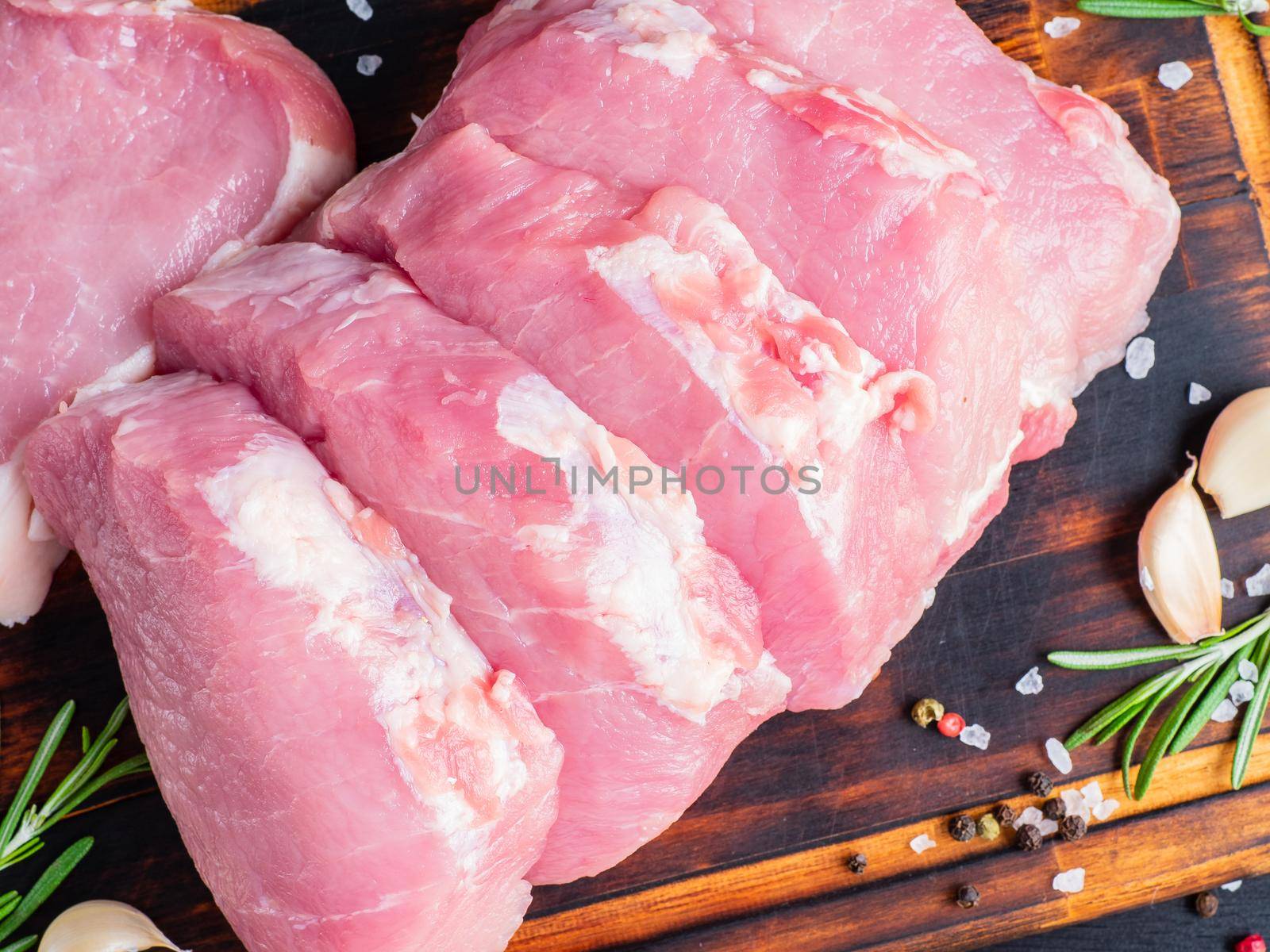Pork steak, raw carbonate fillet on dark background, meat with rosemary, seasonings, top view, close up.