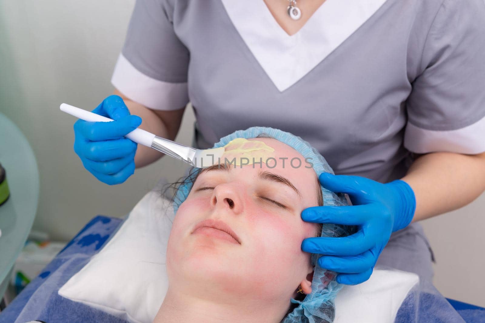 Cosmetologist applies alginate mask with spatula on face of woman. Facial skin and anti-aging treatment. Cosmetology and professional facial skin care.