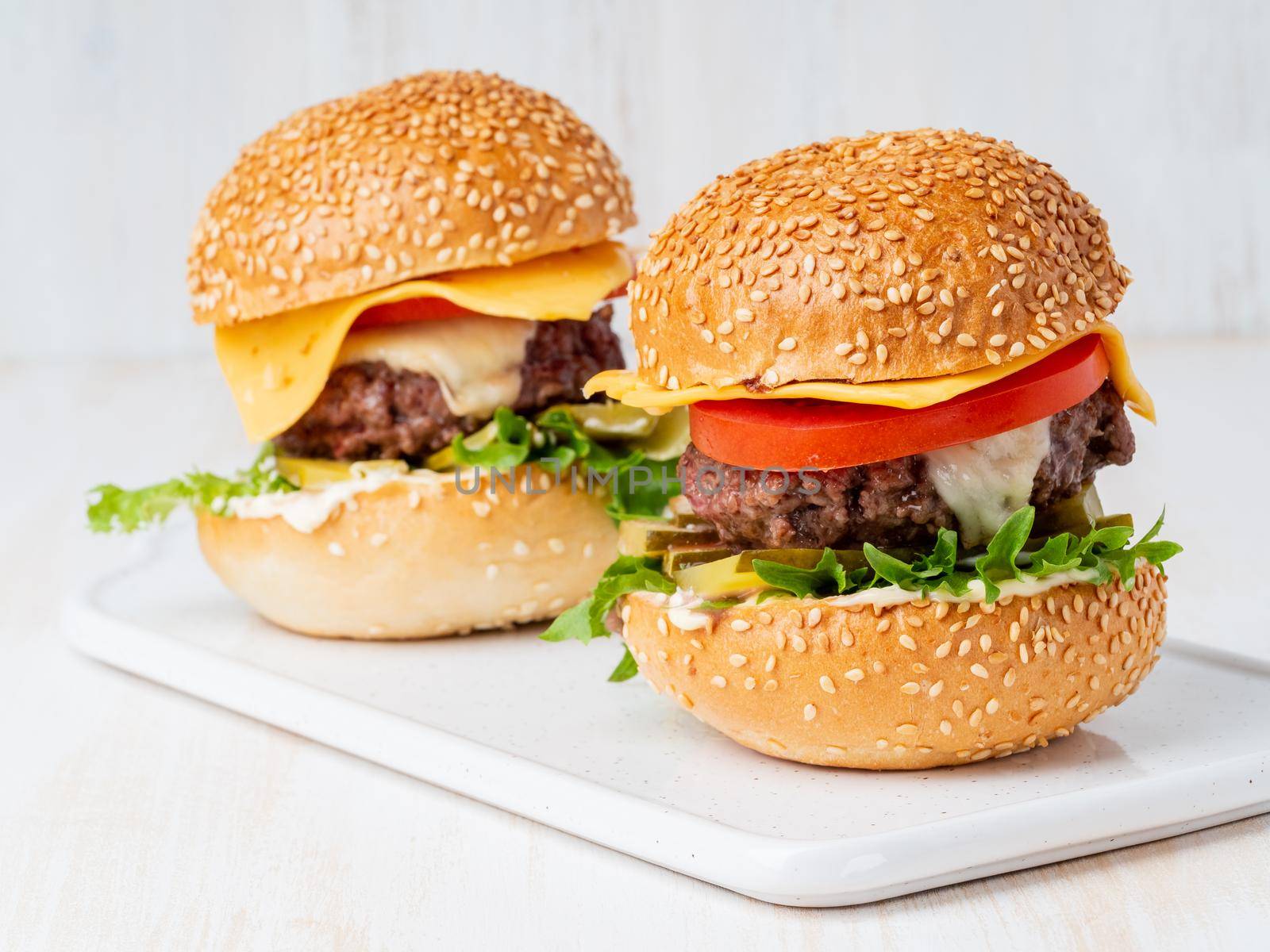 Two hamburgers on white board on white background, hot homemade unhealthy fat food by NataBene