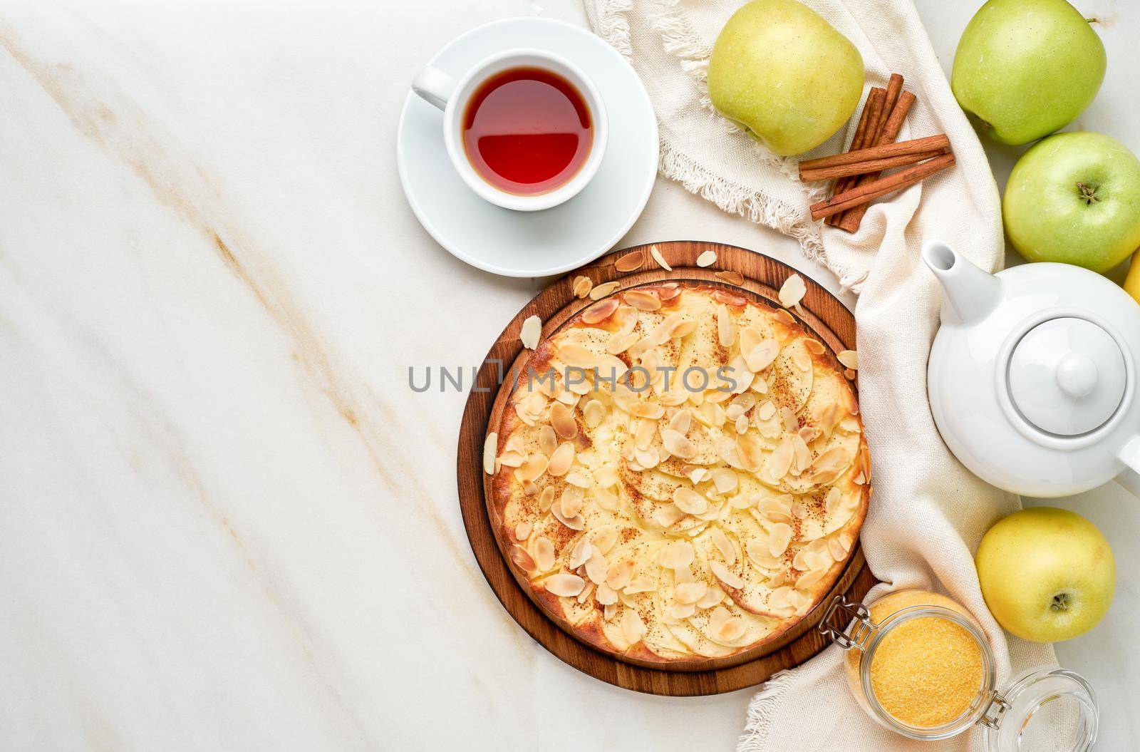 Cheesecake, apple pie, curd dessert with polenta, apples, almond flakes and cinnamon on white marble kitchen table, top view, copy space