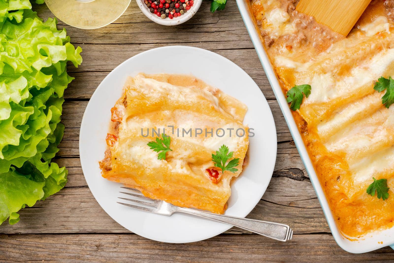 Cannelloni with filling of ground beef, tomatoes, baked with bechamel tomato sauce, top view, old dark wooden background
