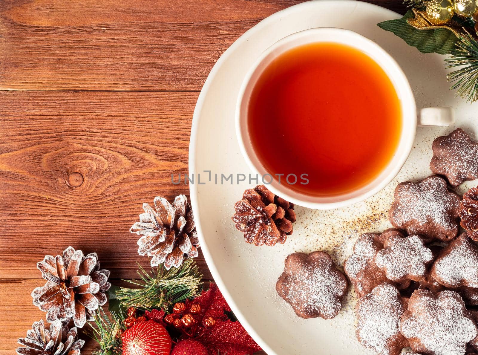 Christmas or new year card. Winter holiday composition, top view, copy space, brown wooden background. Tea, cookies, fir cones, candles