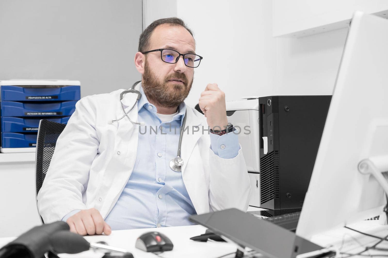 Portrait of friendly smiling healthcare professional therapist sitting at workplace. Happy confident male doctor physician wearing white medical coat and stethoscope. High quality photo