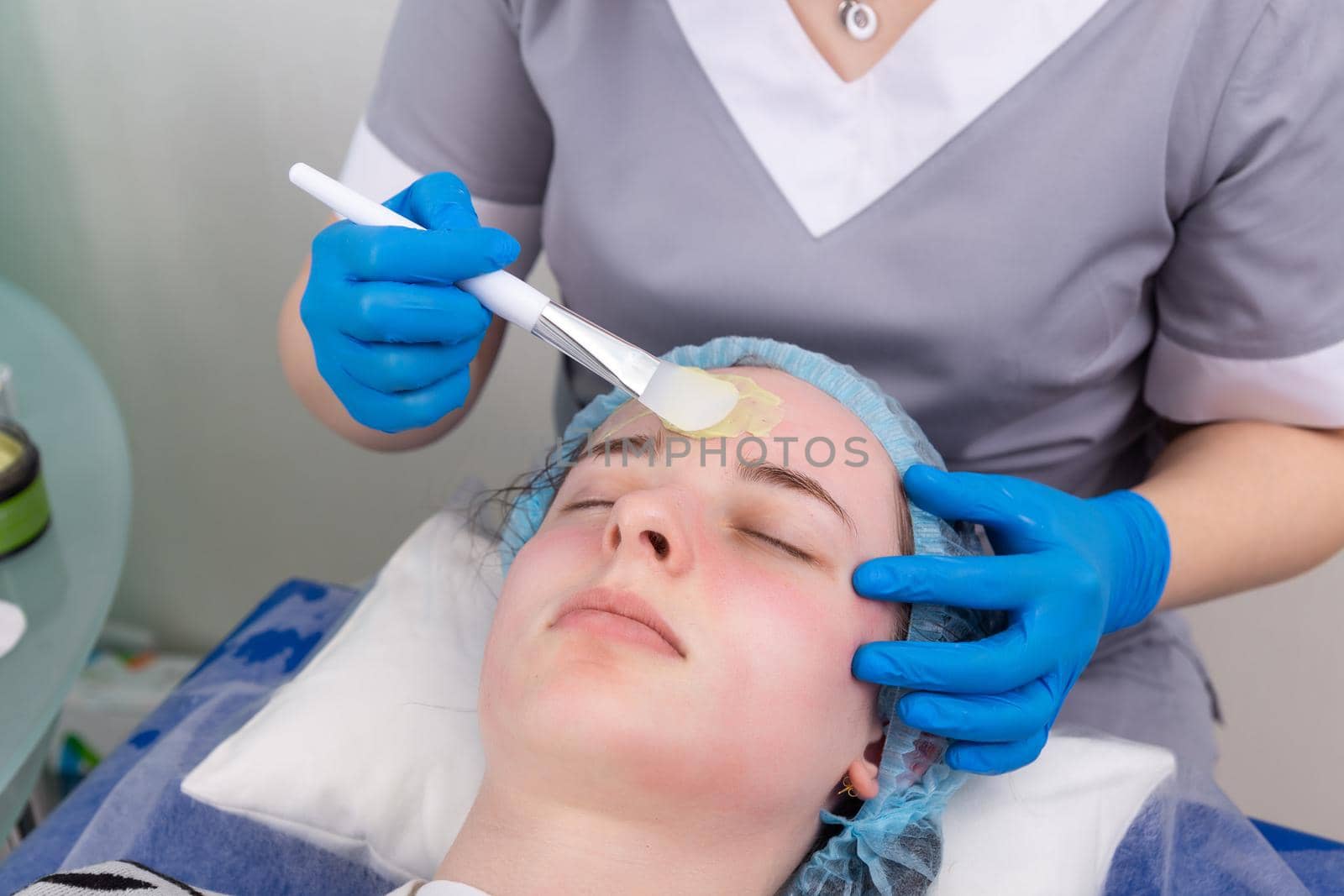 Cosmetologist applies alginate mask with spatula on face of woman. by BY-_-BY