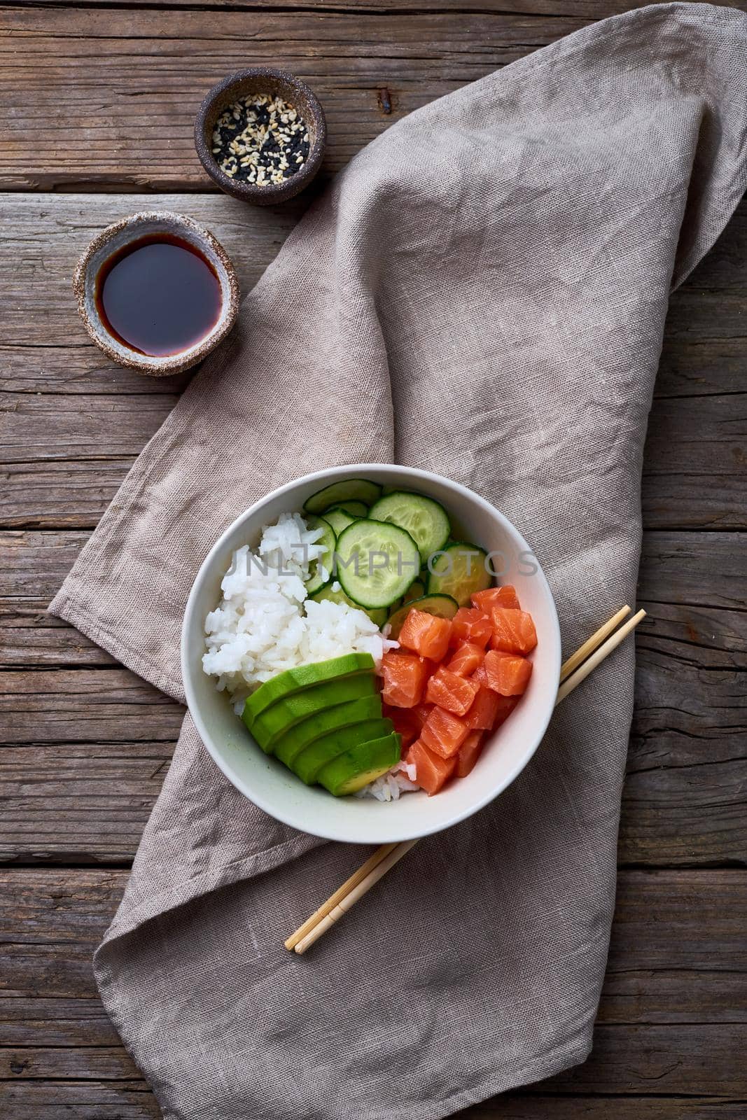 salmon poke bowl with fresh fish, rice, cucumber, avocado with black and white sesame. Food concept, top view, vertical