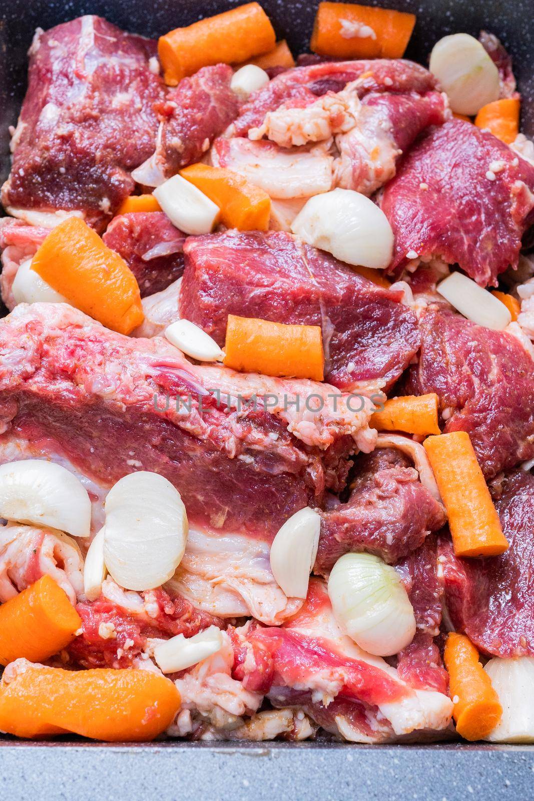 lamb meat on a baking sheet marinated with spices, vegetable oil, carrots and onions ready for baking in the oven by olex