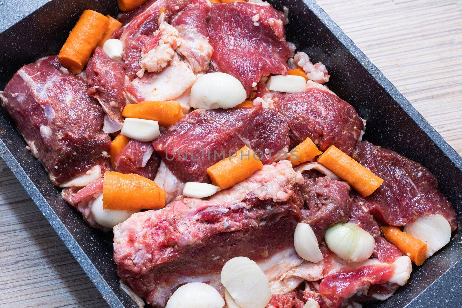 lamb meat on a baking sheet marinated with spices, vegetable oil, carrots and onions ready for baking in the oven or roasting