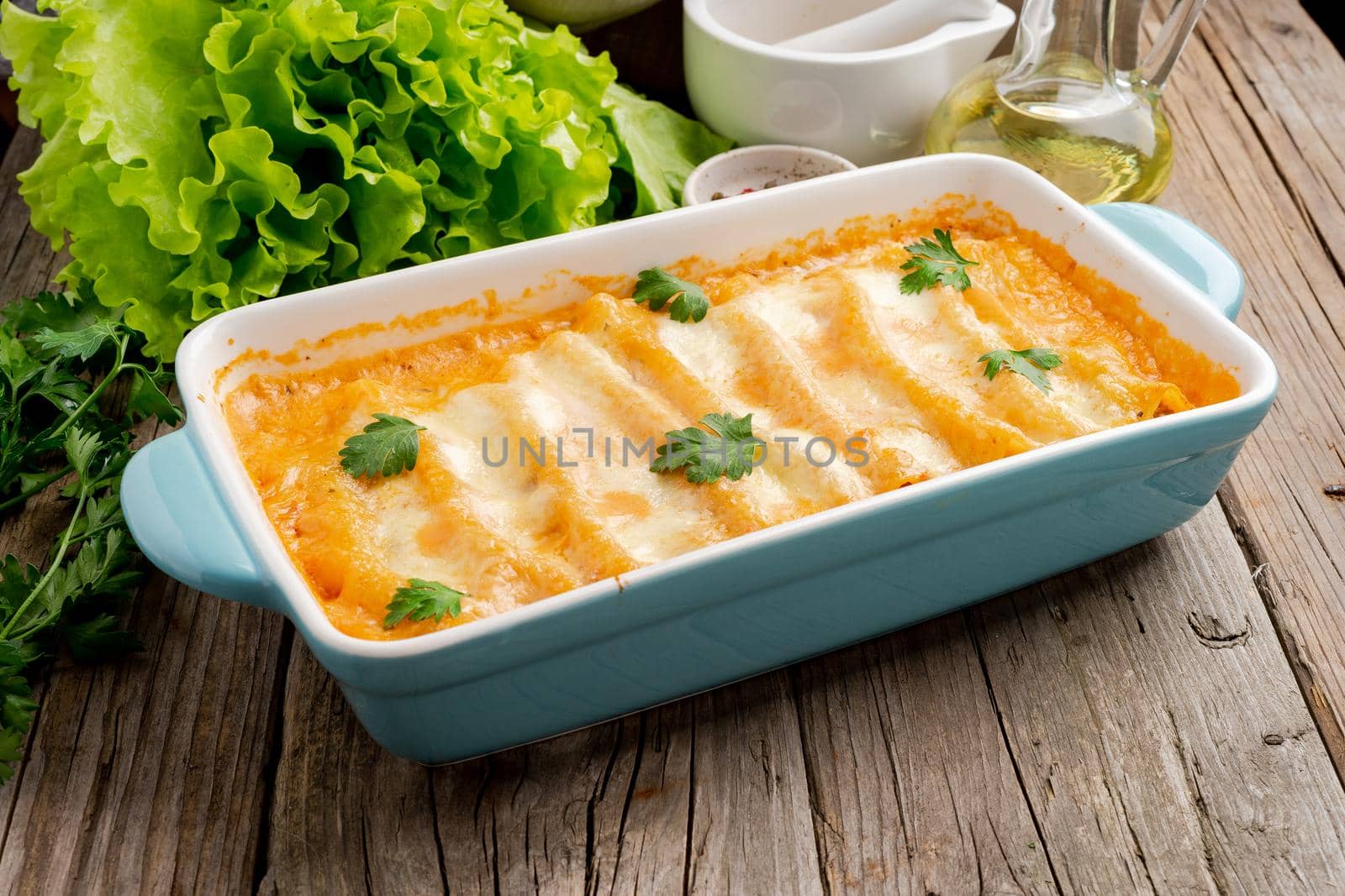 Cannelloni with filling of ground beef, tomatoes, baked with bechamel tomato sauce, side view, old dark wooden background