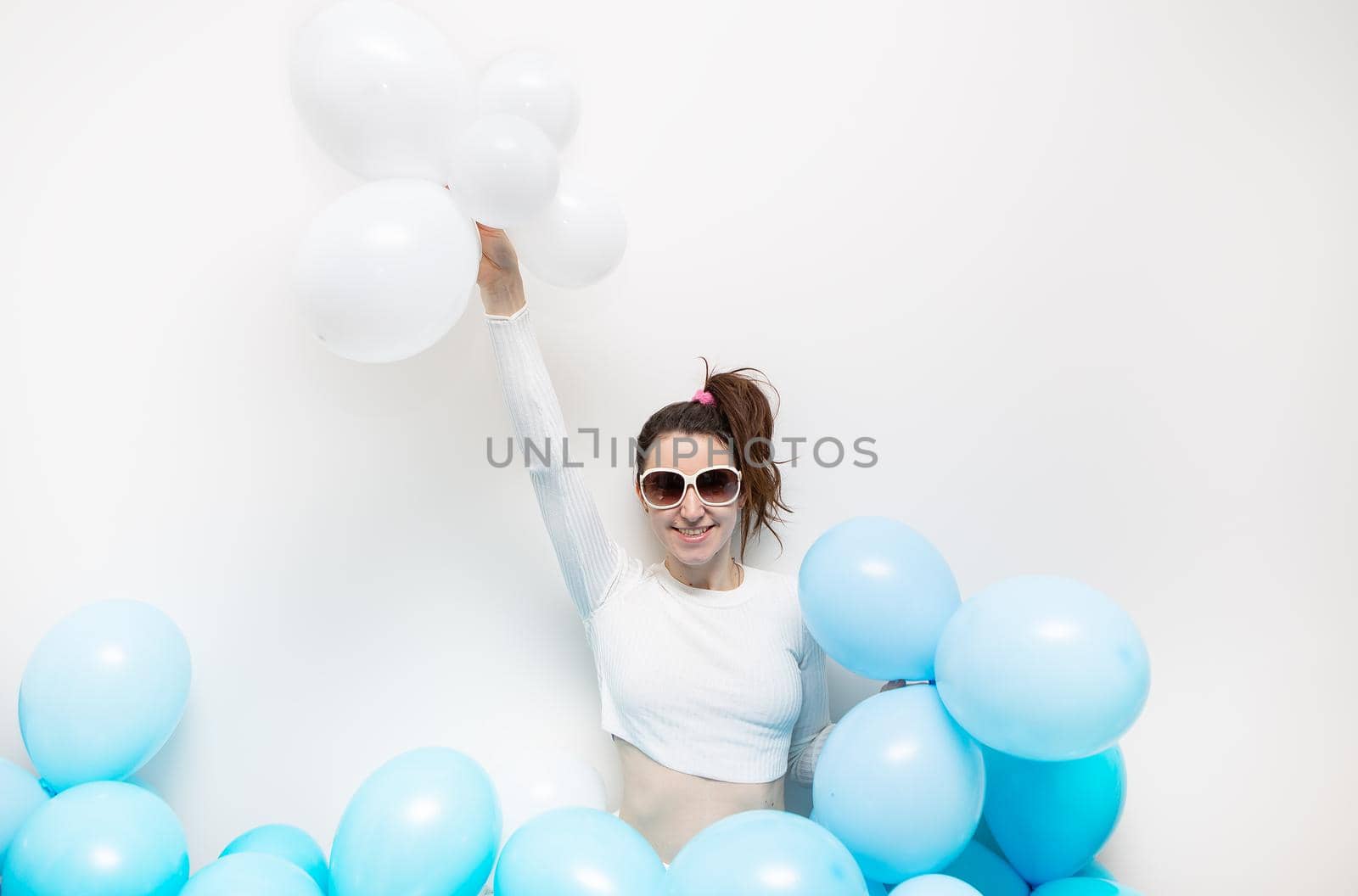 Happy girl in glasses smiles and holds blue balloons in her hands. Place for an inscription, holiday concept. Birthday