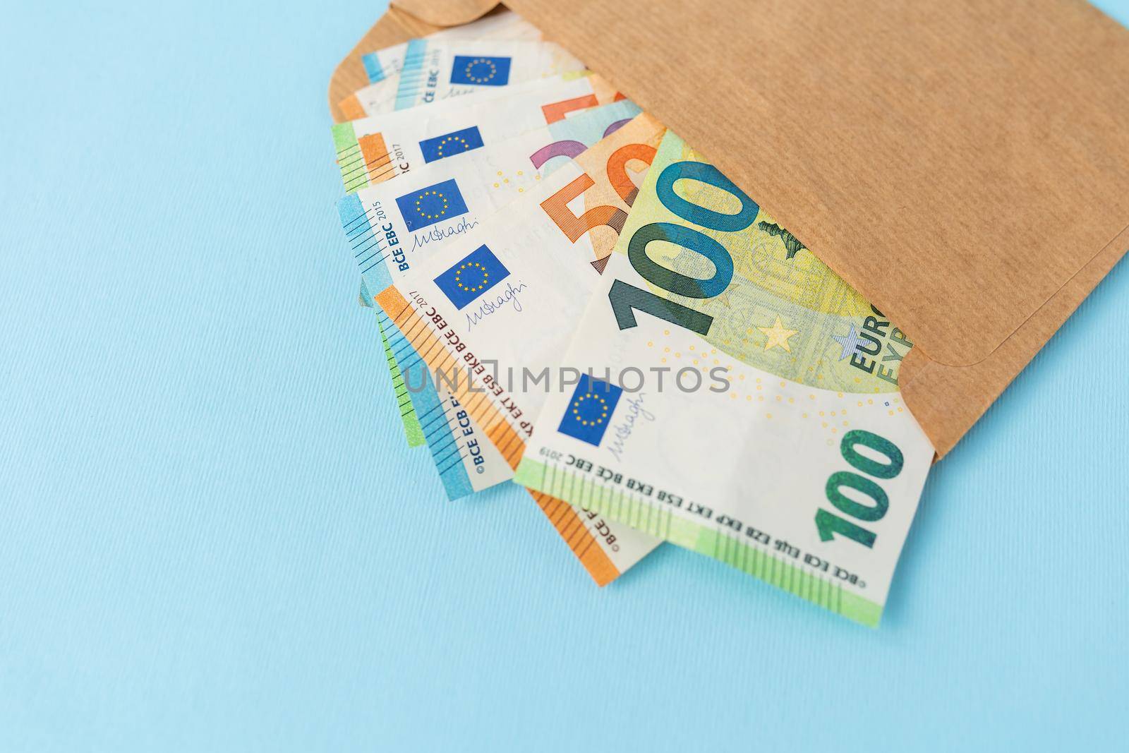 A cache of euro money, in banknotes of 100 denominations, coming out of an envelope on a blue background. The concept of salary, bribe, loan, debt, win