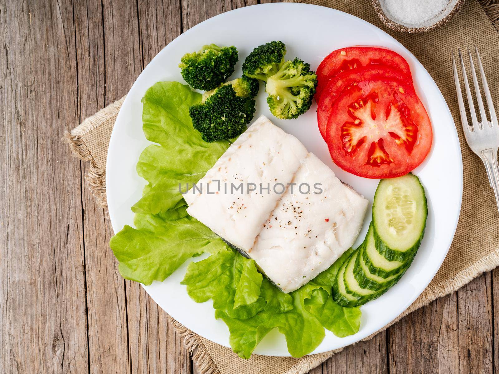 Steamed cod fish. Paleo, keto, fodmap healthy diet with vegetables on white plate on wooden table, top view