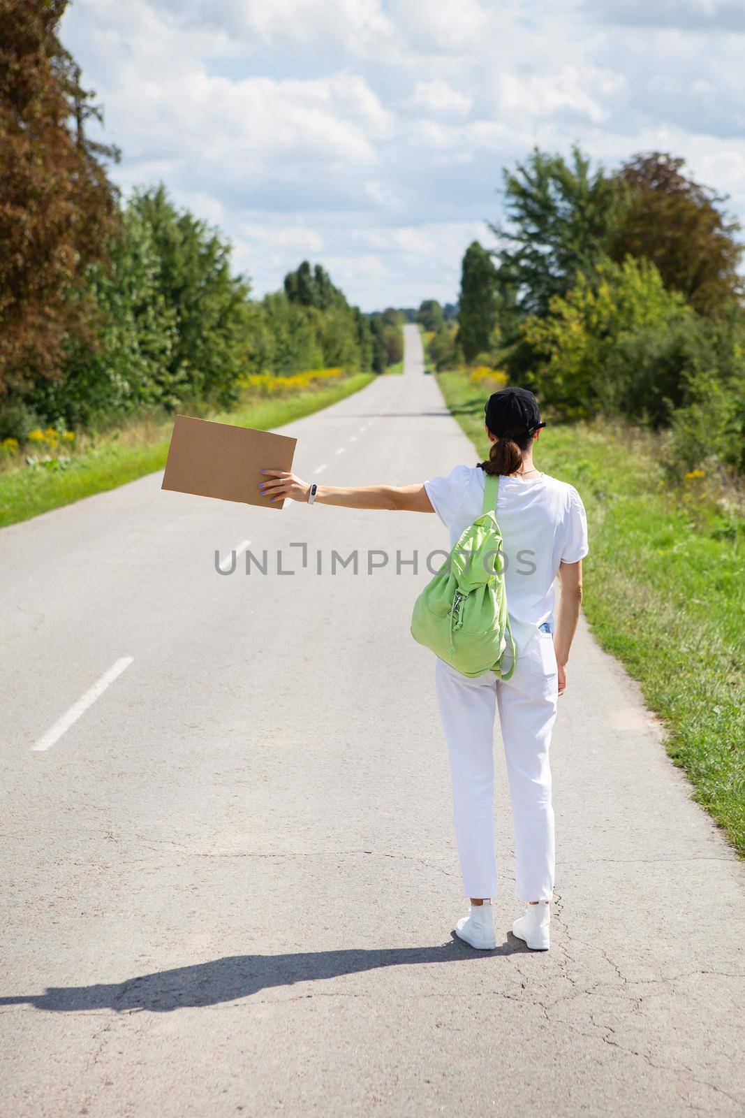 A beautiful girl with a backpack on her shoulder stands on the road brakes the car, hitchhiking, adventure, tourism, alone