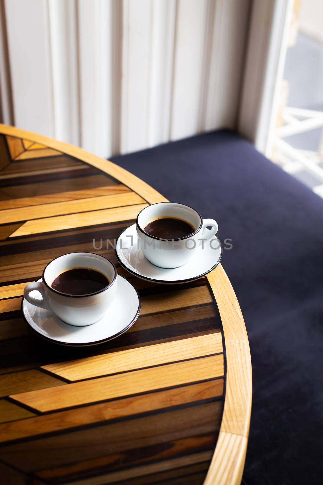 Two modern cups of espresso on a wooden table, a table in front of the window. Coffee break