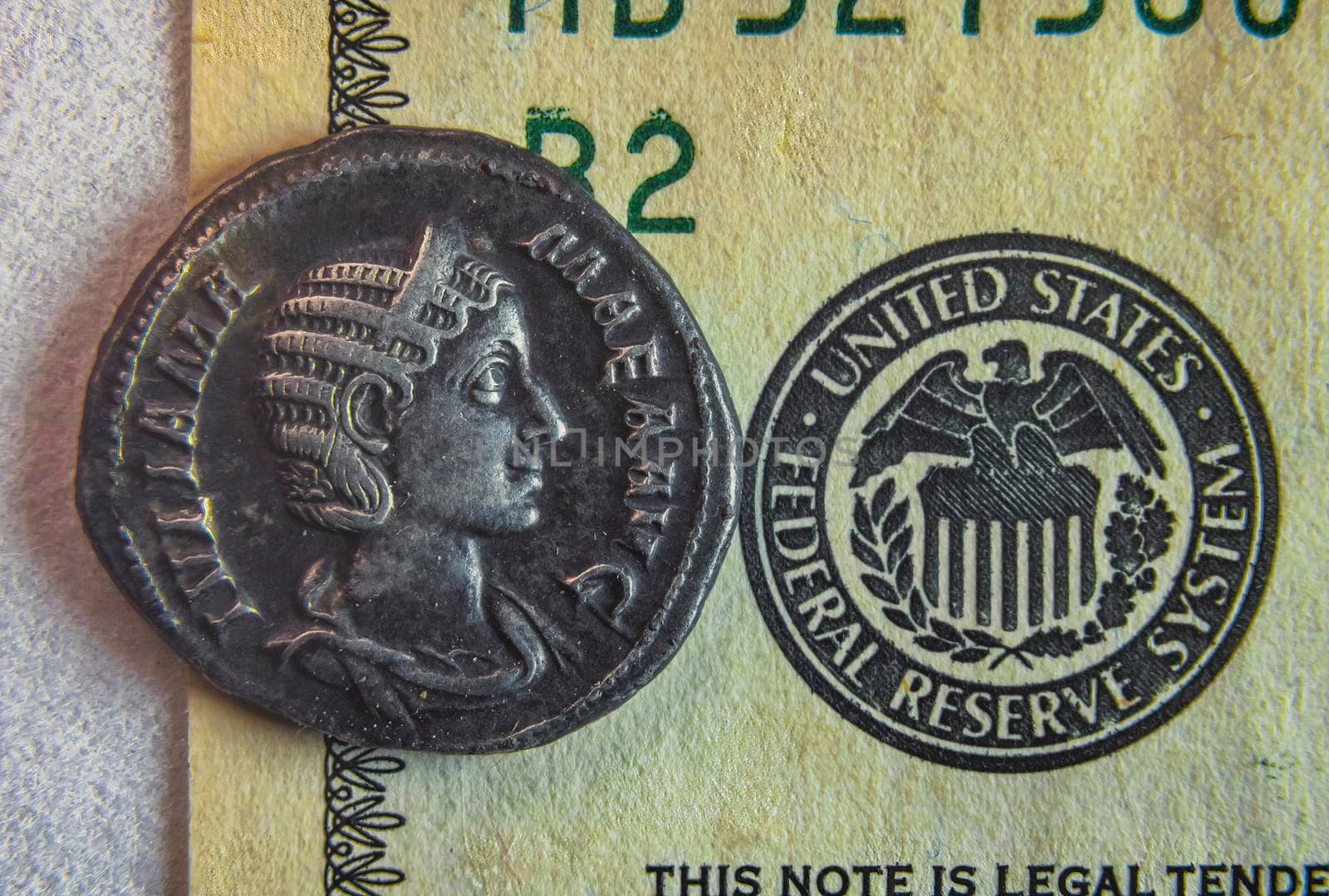 An old Roman coin lies on a 100 dollar bill near the badge with an eagle