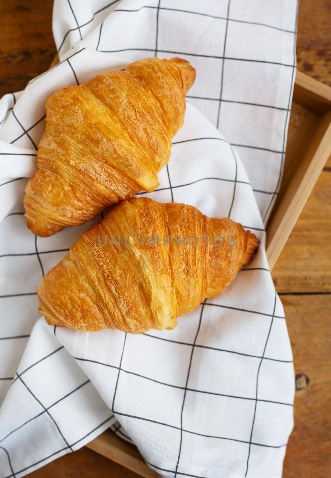 Breakfast in bed, fresh croissants and a cup of coffee on a wooden tray. Fine morning