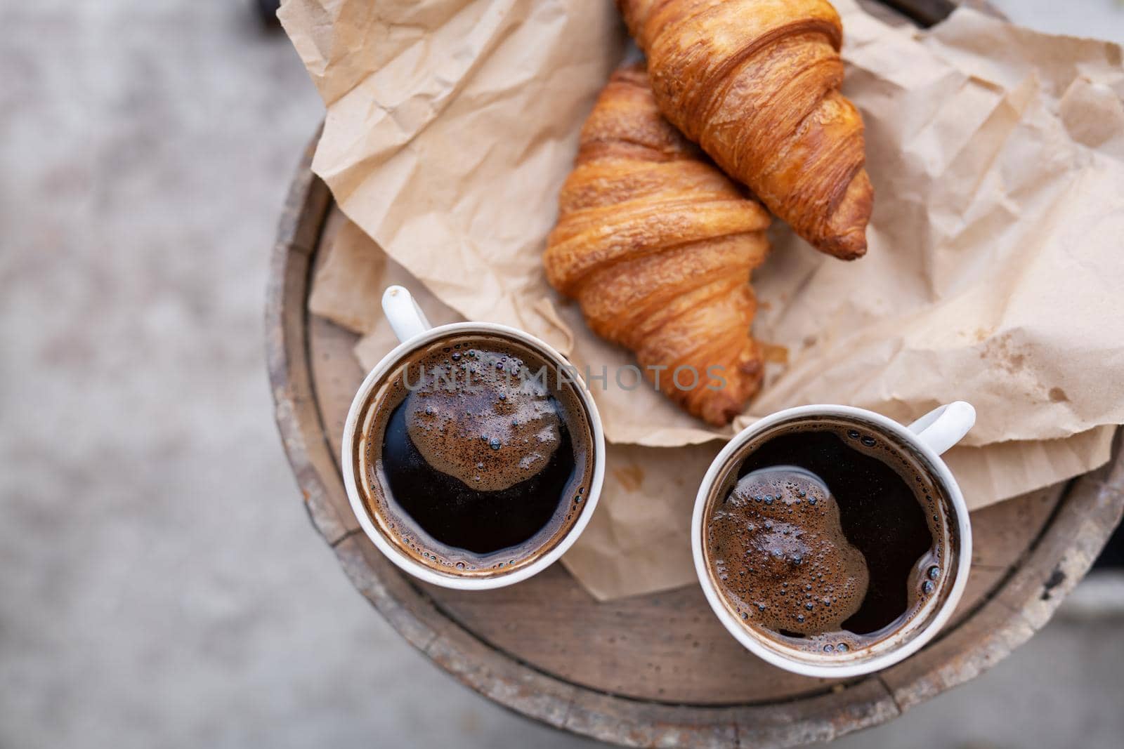 There are two cups of coffee and croissants on craft paper on a wooden barrel. Retro style. by sfinks