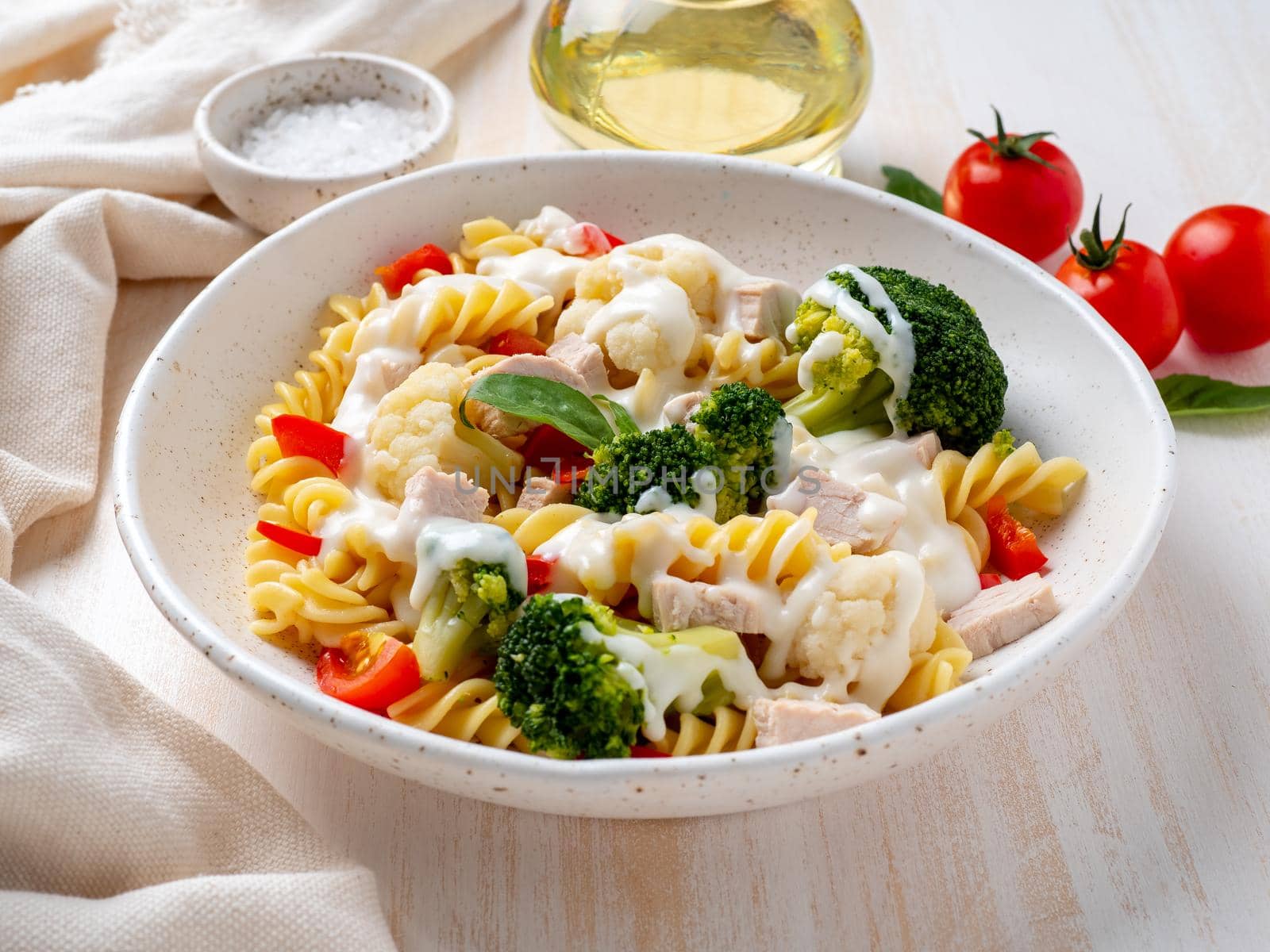 Pasta fusilli with vegetables and boiled steamed meat, white sauce on white wooden table, low-calorie diet, low-fat diet, side view
