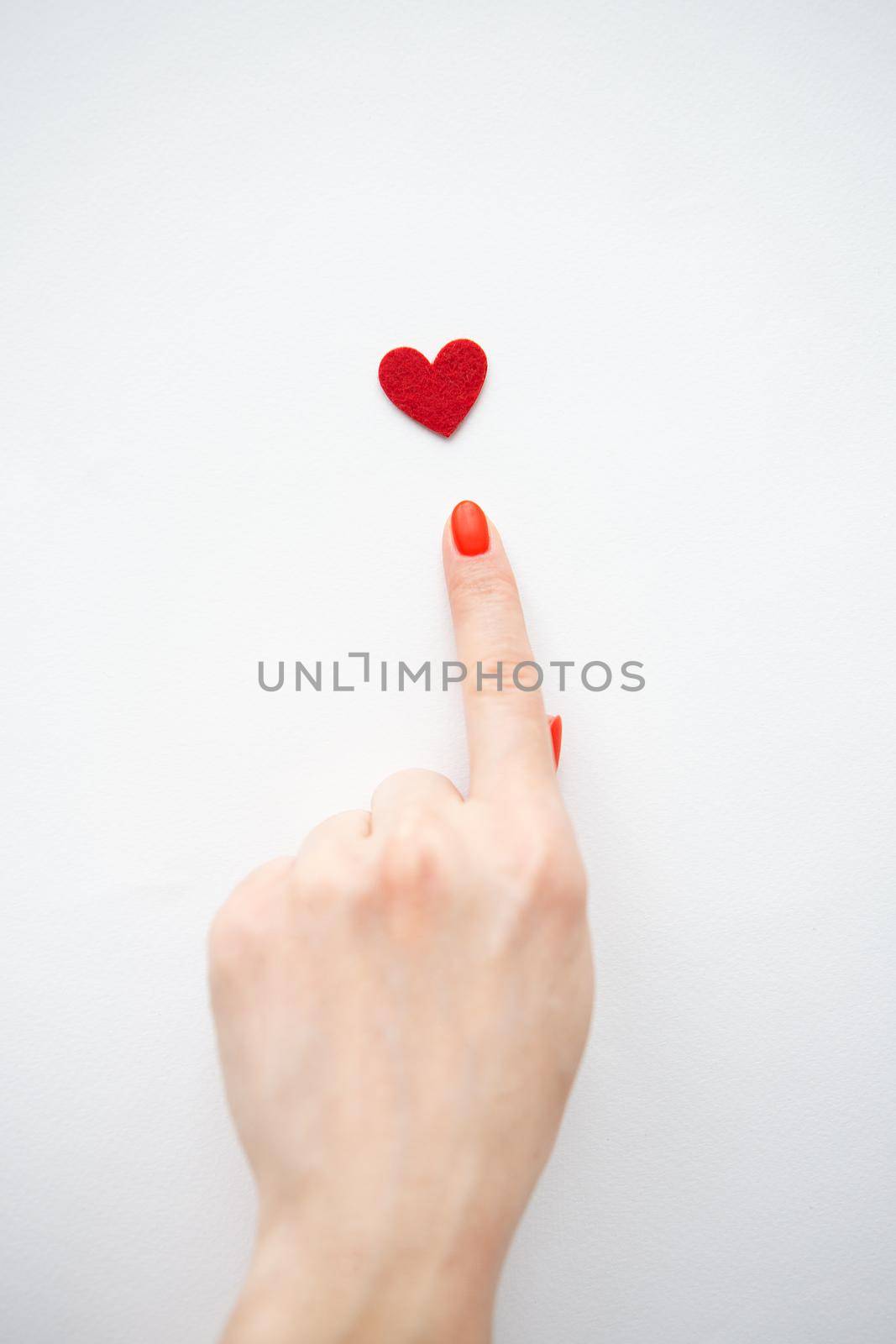 The girl points with her hand to a small red heart. The concept of care and love