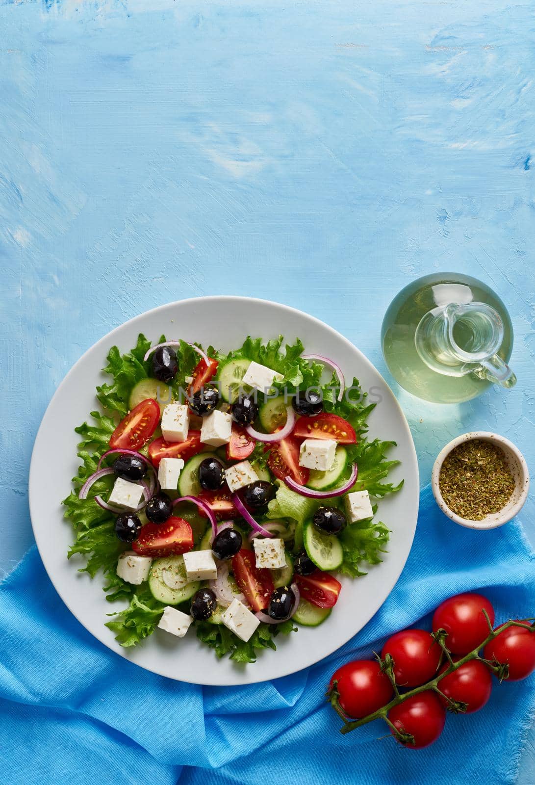 Greek salad on white plate on bright blue table, top view, copy space