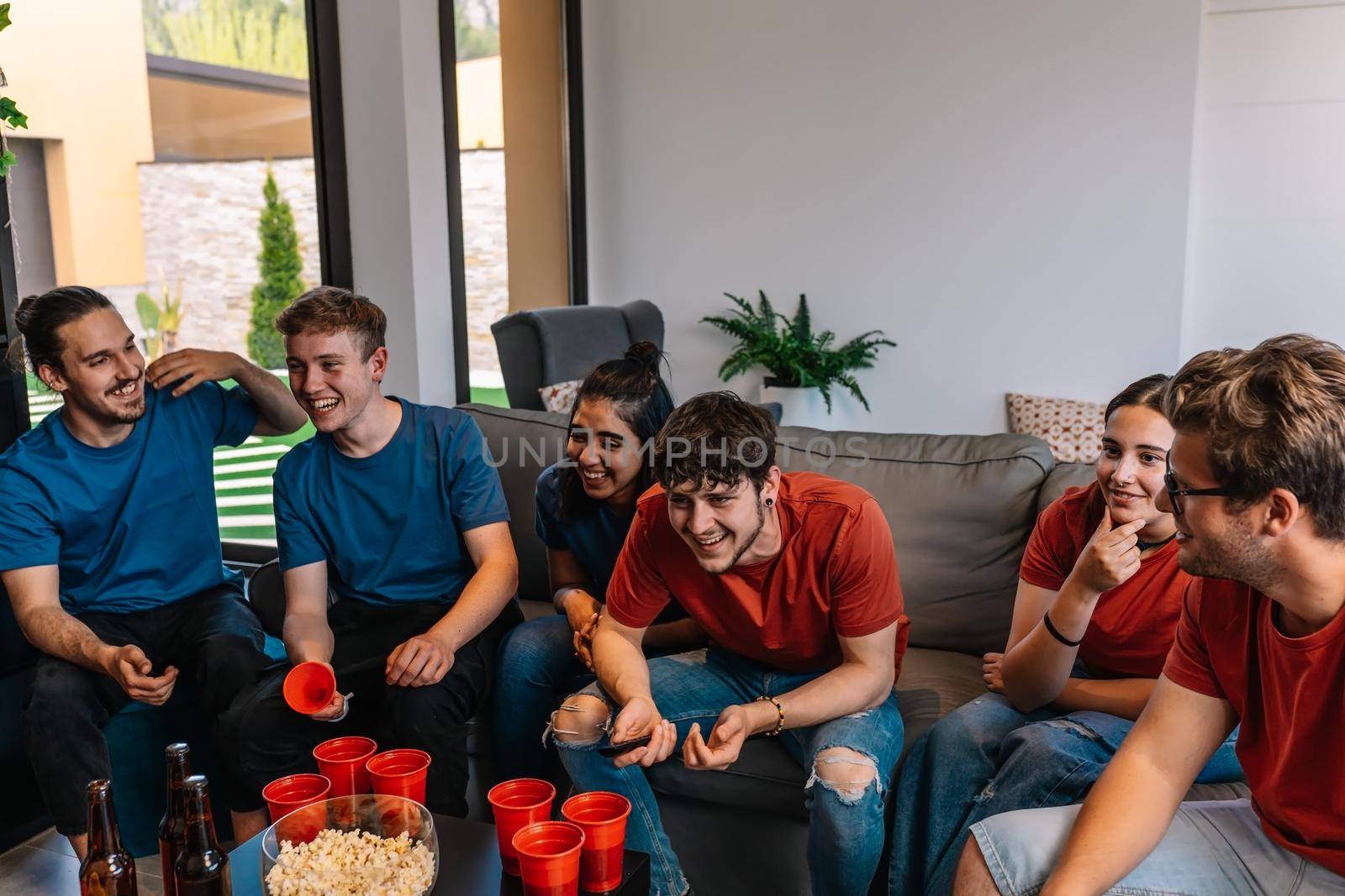 friends watching a football match on television and competing for their team. group of young people at a party. by CatPhotography