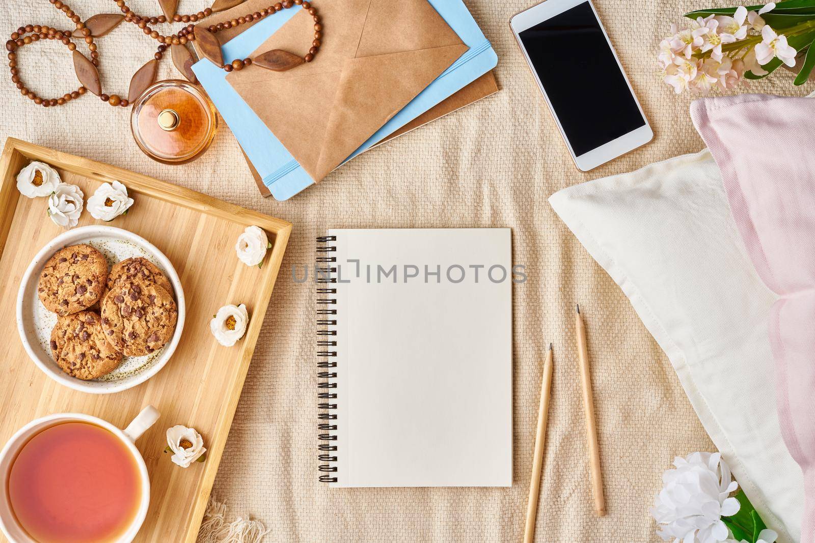 Mockup with notepad on bed and women's accessories, tea, cookies, pillows, flowers, letter, notebook. Cozy women's creative world.