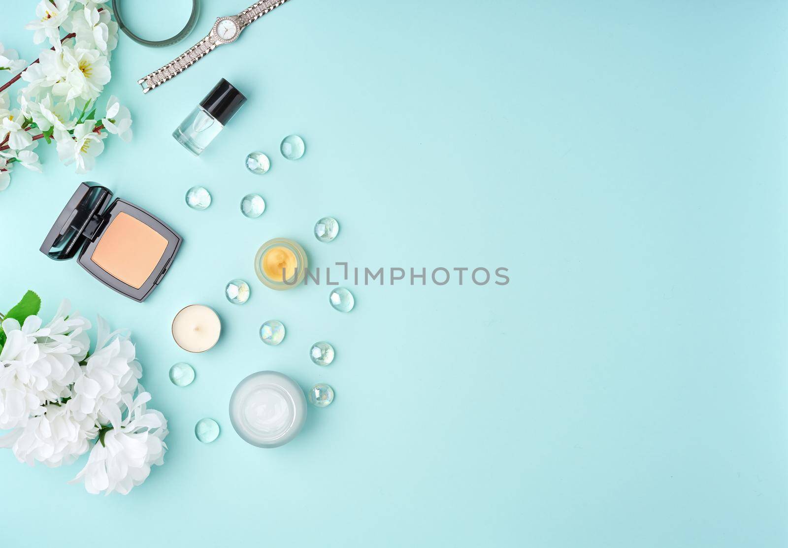 Flat lay woman accessories with cosmetic, facial cream, bag, flowers on pastel blue table. by NataBene