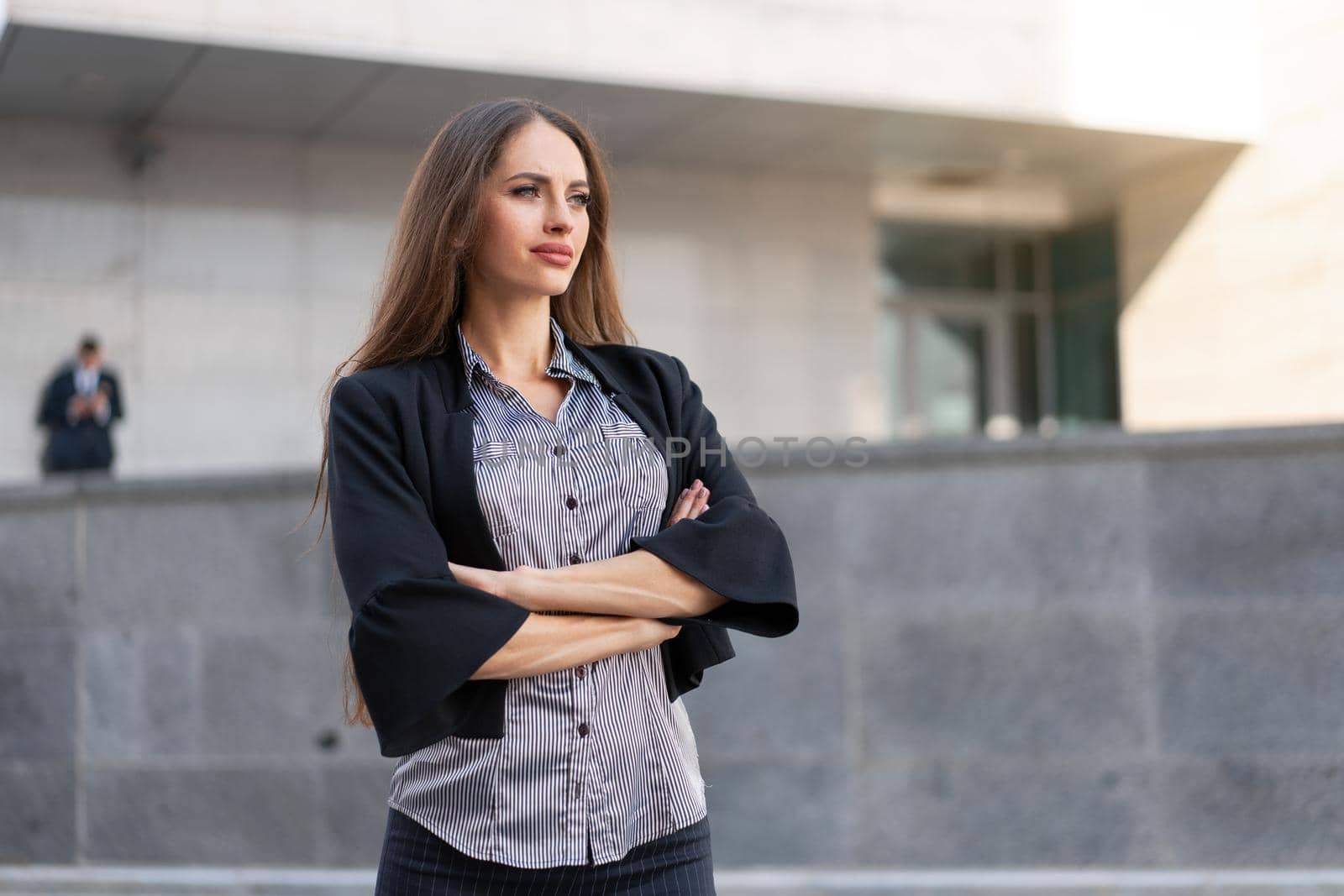 Business woman with long hair dressed black jacket standing outdoor near corporate office building hand folded Beautiful caucasian female business person portrait city street Side view looking away