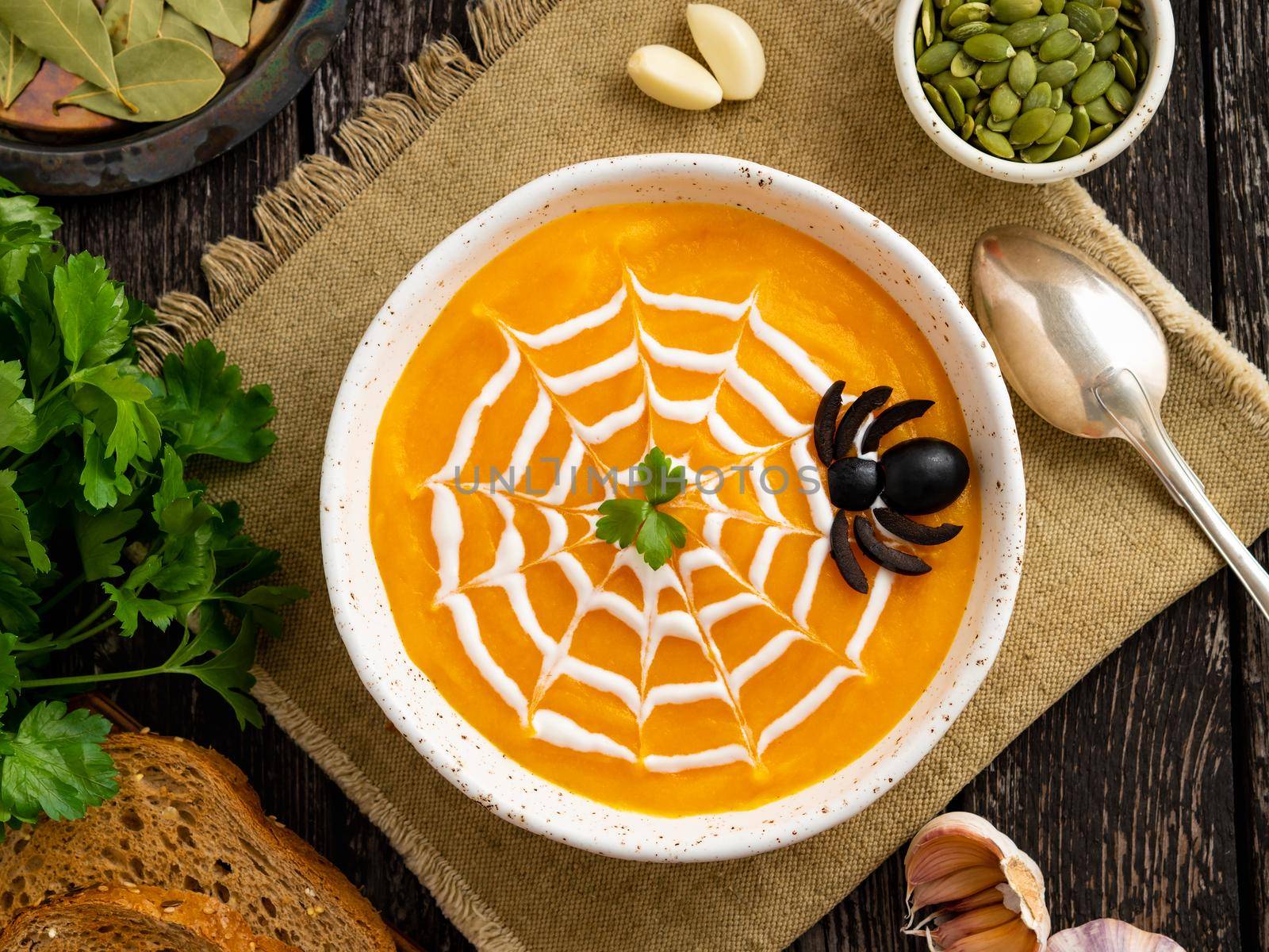 Funny food for Halloween. Pumpkin puree soup, spider web, dark old wooden table, top view. by NataBene