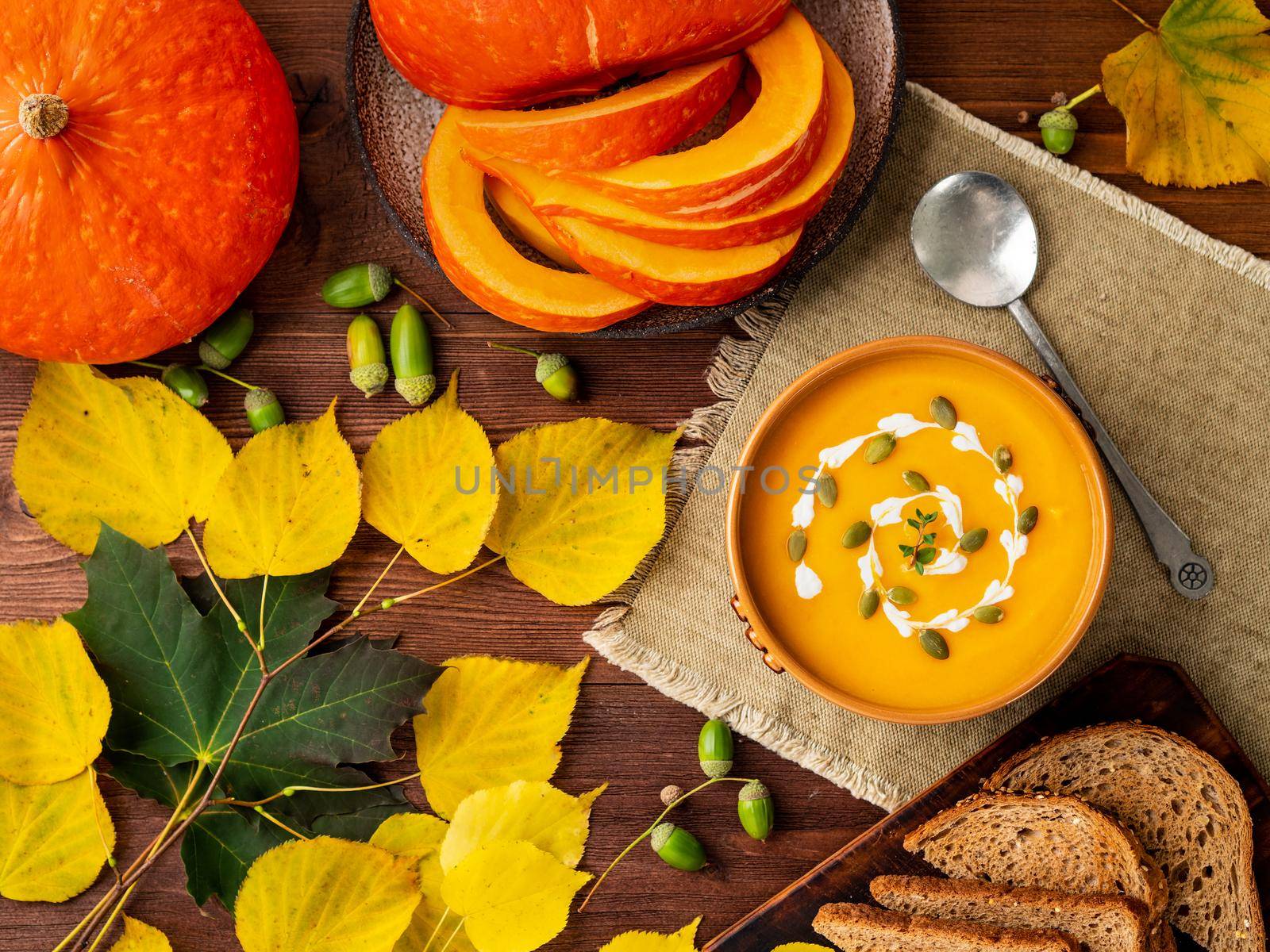 Autumn food. Pumpkin puree soup, leaves, dark brown old wooden table, top view. by NataBene
