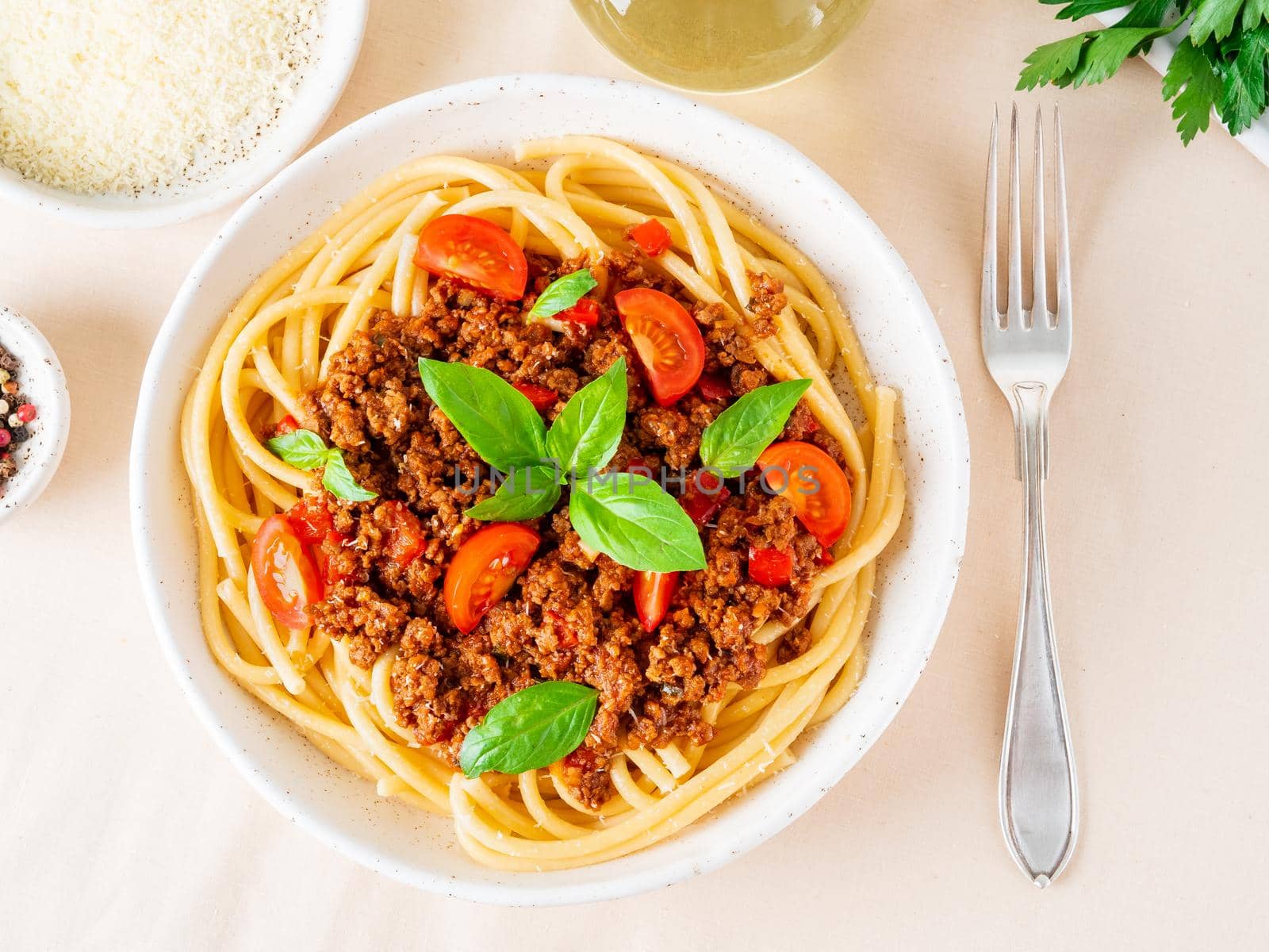 pasta bolognese with tomato sauce, ground minced beef, basil leaves on white table, linen napkin, top view