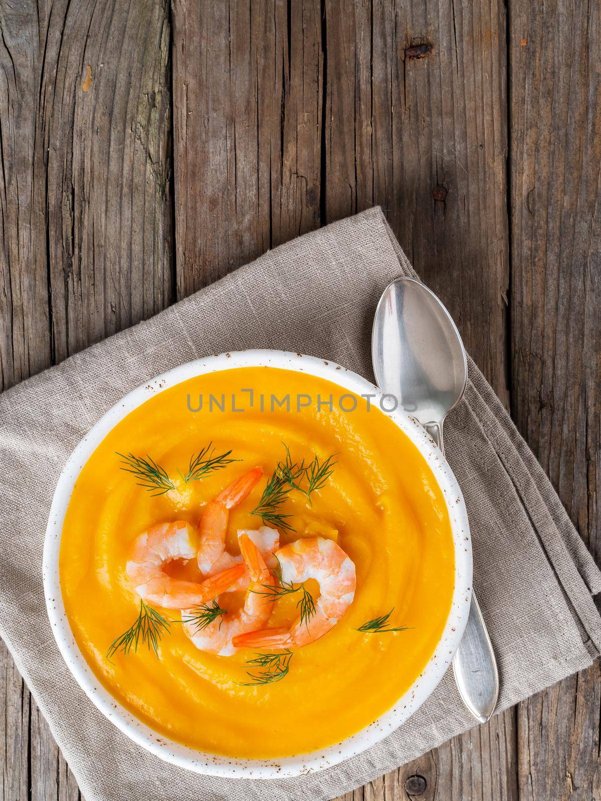 Delicious yellow pumpkin cream soup with shrimp on dark gray old rustic wooden table, top view, copy space, vertical.