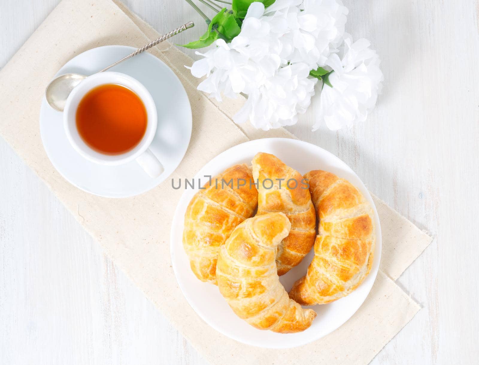 Cup of tea, flowers and a fresh baked puff pastry on a white table. Delicious croissants, top view